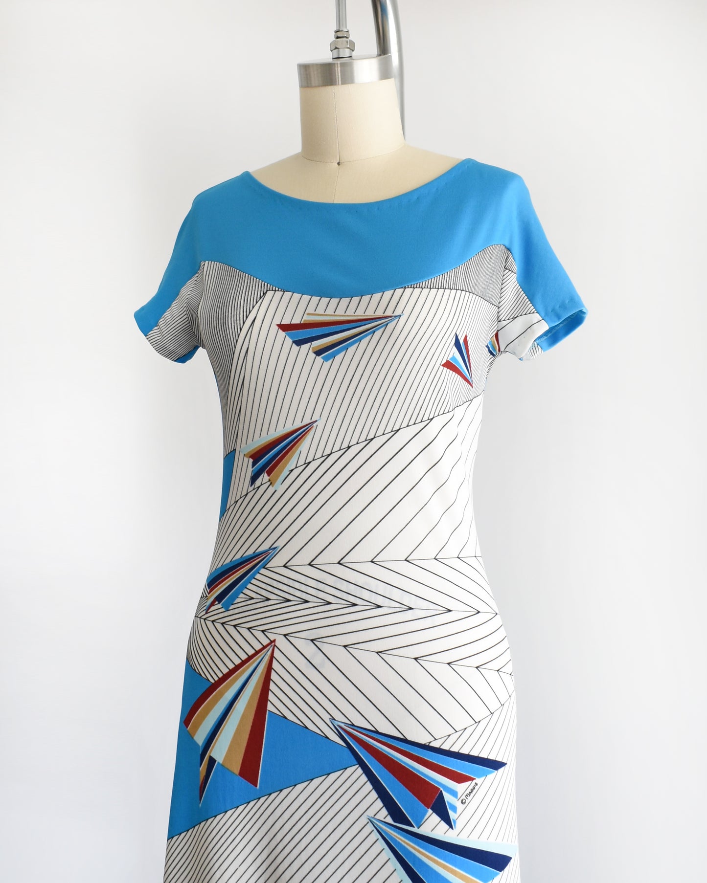 side front view of a vintage 1970s dress with geometric patterns and paper planes on a mannequin against a white background