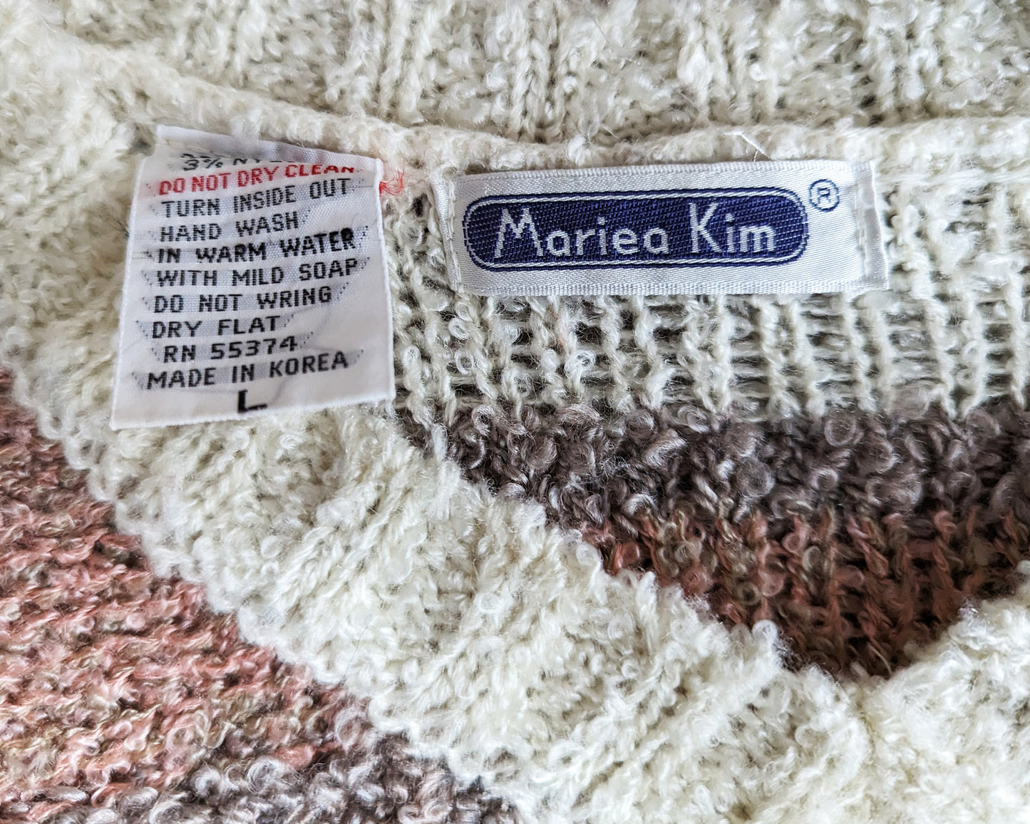 Close up of the tag which says Mariea Kim. It also has a care tag that says the machine washable instructions, along with a L size, even though this sweater would best fit a medium