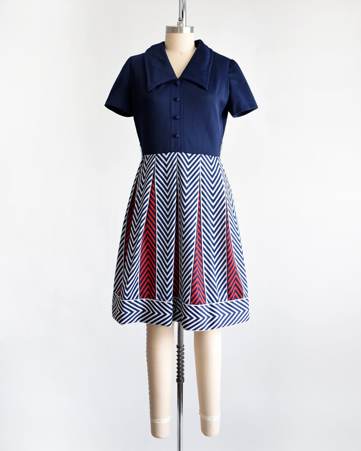 a vintage 1970s navy blue, white, and red dress with a chevron patterned skirt on a mannequin against a white background