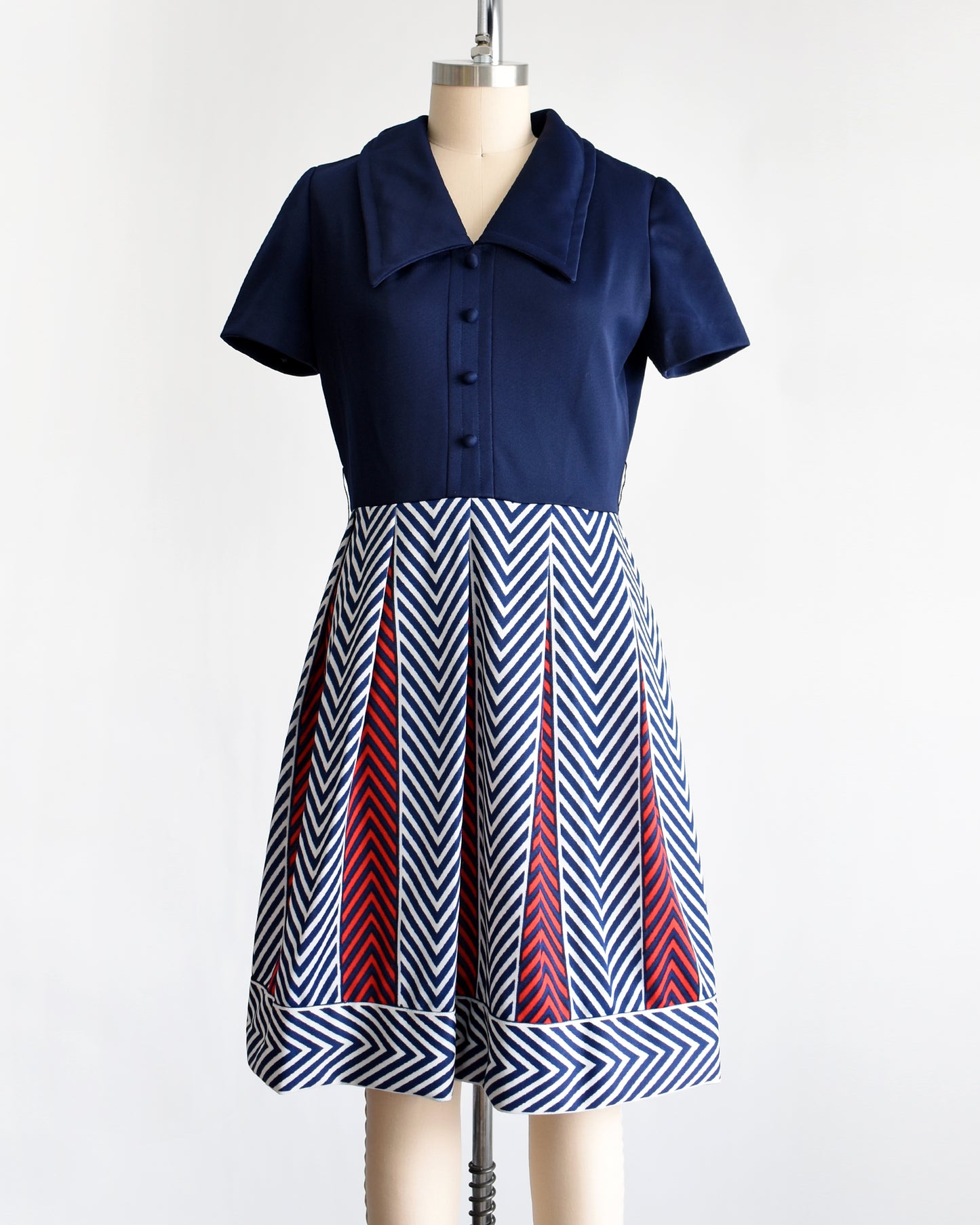 a vintage 1970s navy blue, white, and red dress with a chevron patterned skirt on a mannequin against a white background