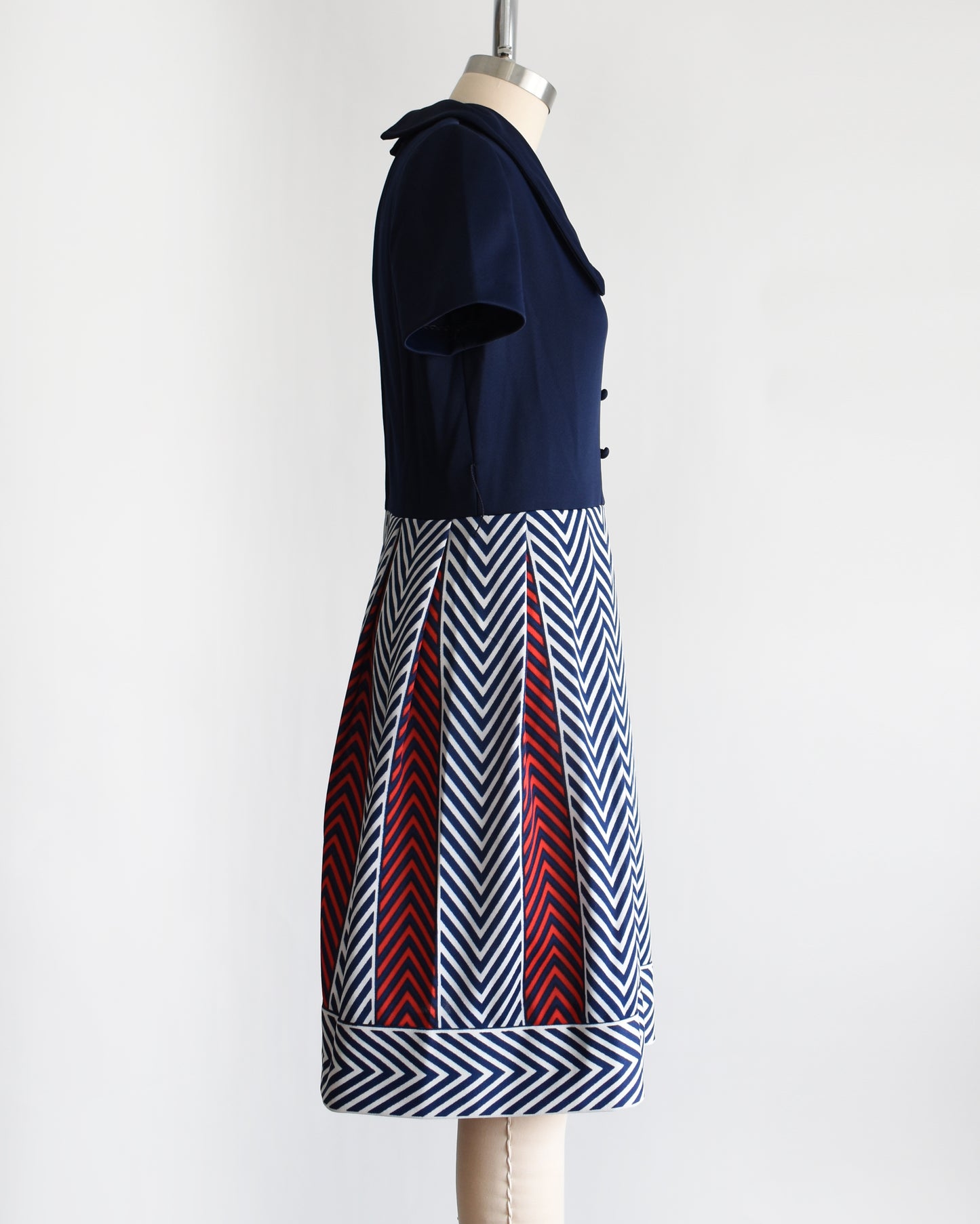 side view of a vintage 1970s navy blue, white, and red dress with a chevron patterned skirt on a mannequin against a white background