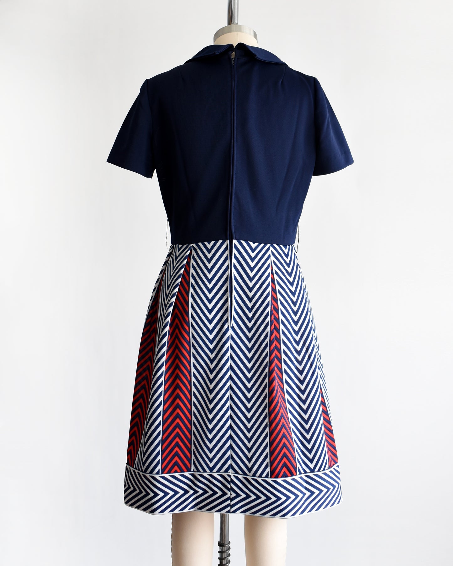 back view of a vintage 1970s navy blue, white, and red dress with a chevron patterned skirt on a mannequin against a white background