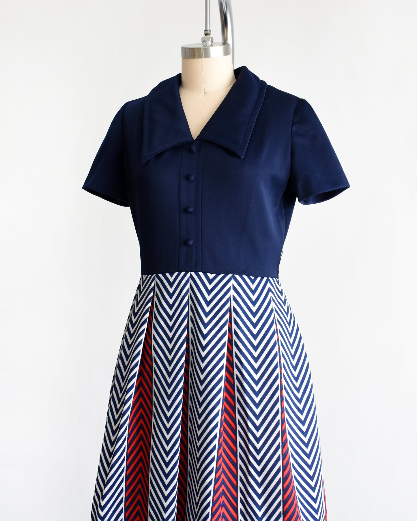 side front view of a vintage 1970s navy blue, white, and red dress with a chevron patterned skirt on a mannequin against a white background