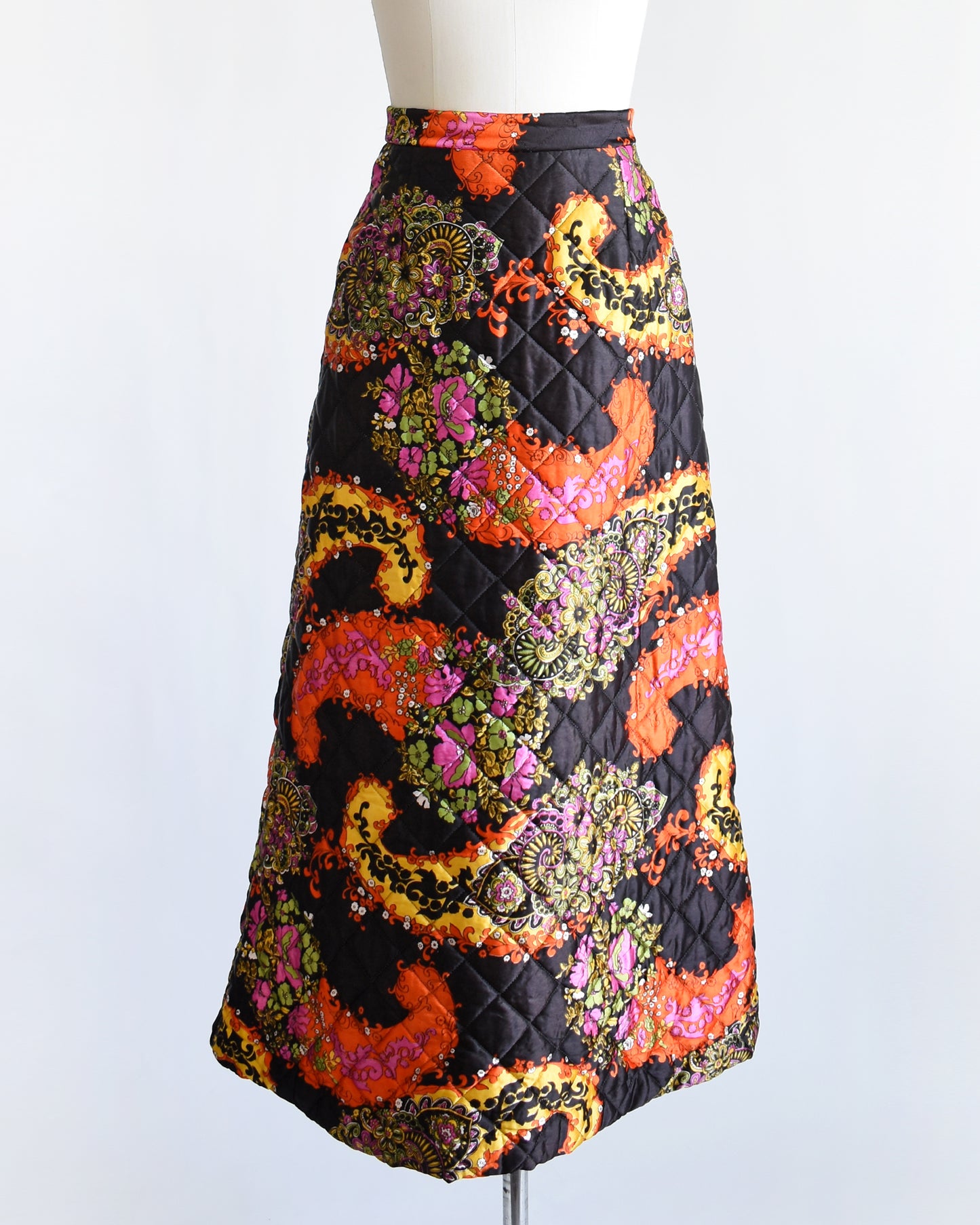a vintage 1970s black quilted skit that has a colorful floral and paisley print on a mannequin against a white background
