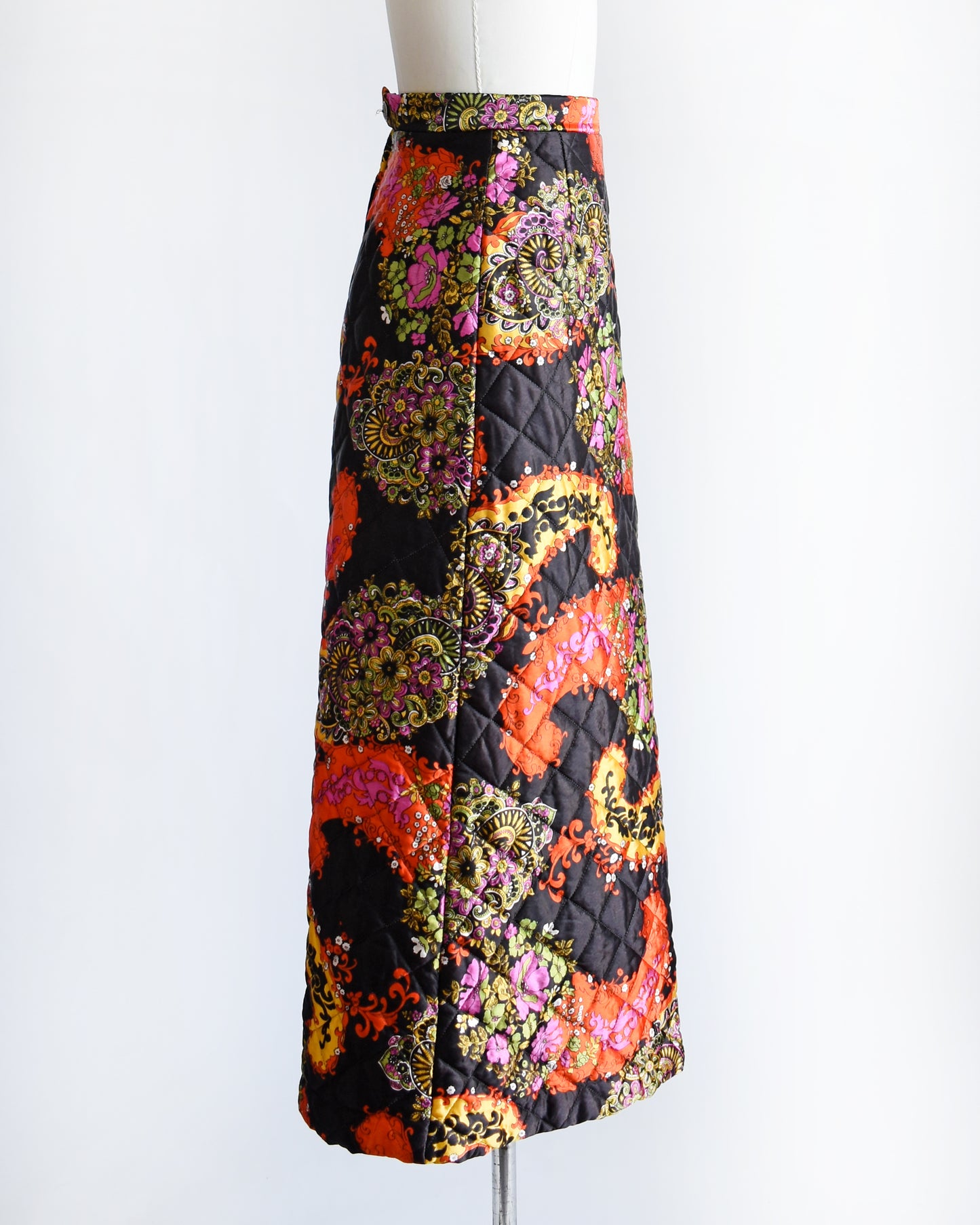 side view of a vintage 1970s black quilted skit that has a colorful floral and paisley print on a mannequin against a white background