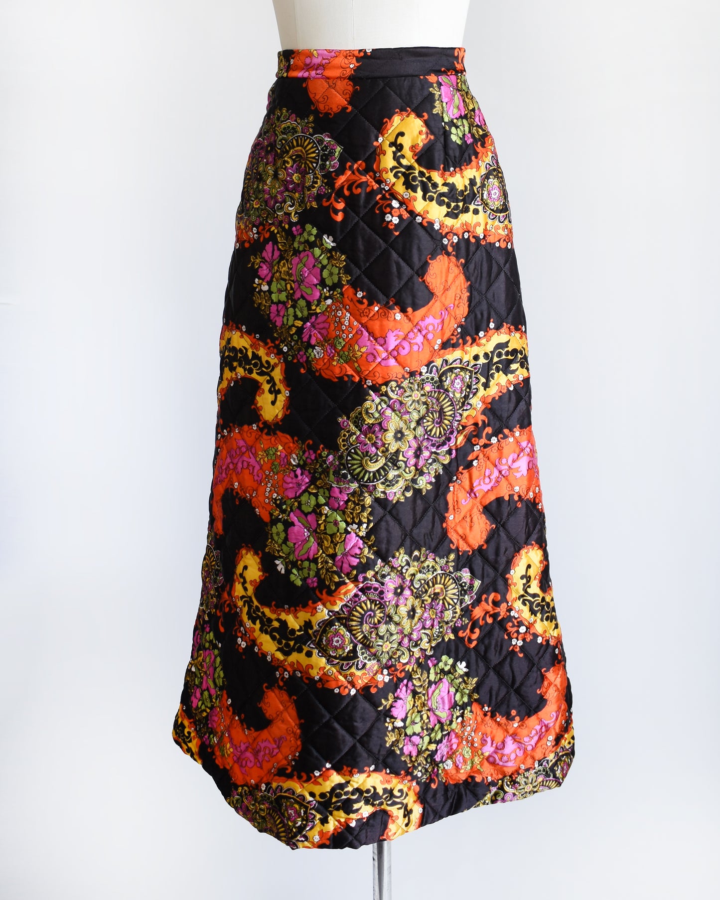 side front view of a vintage 1970s black quilted skit that has a colorful floral and paisley print on a mannequin against a white background