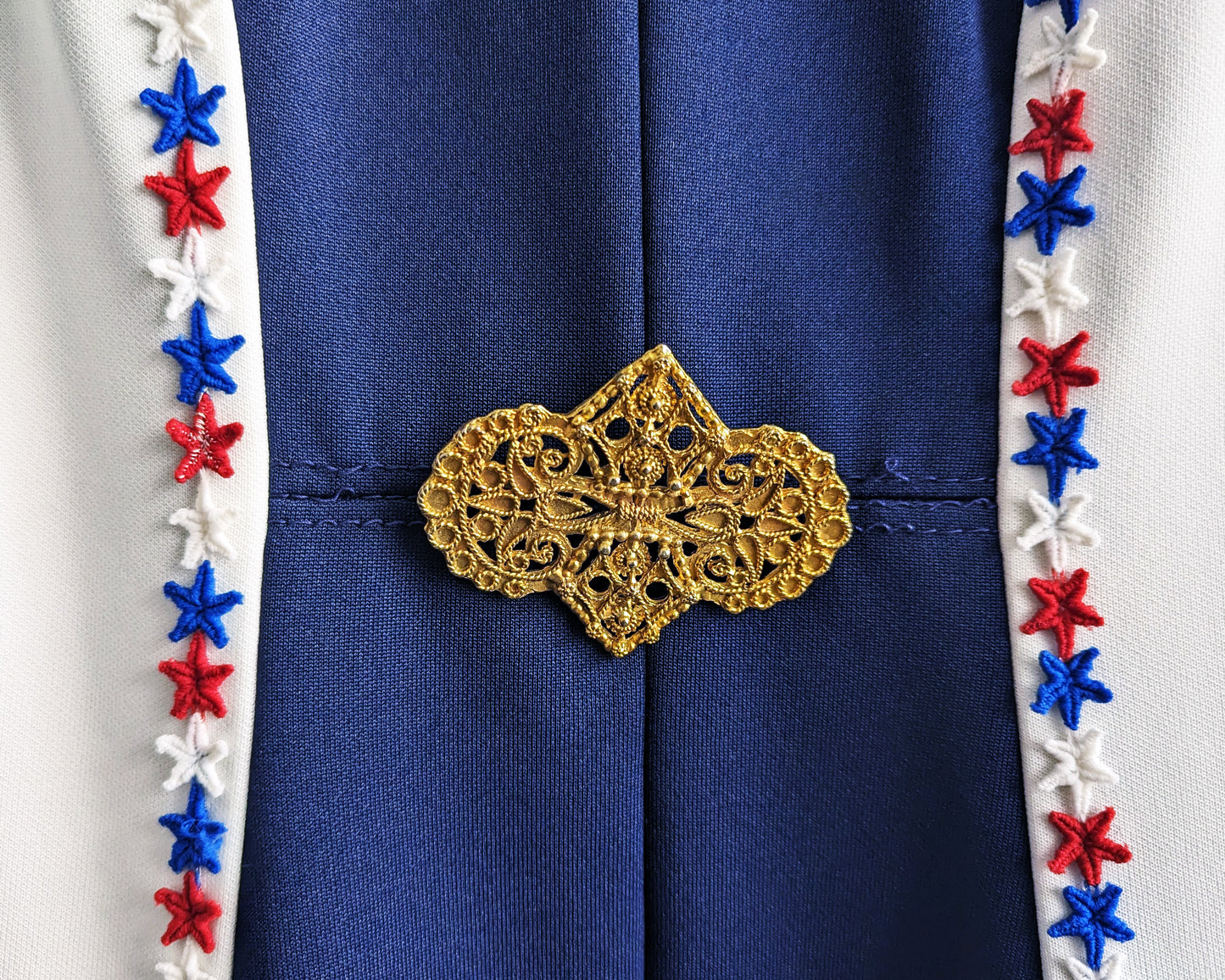A close up of the gold tone brooch at the waist. Also there are a few loose threads along the waistline, but the seam is secure.