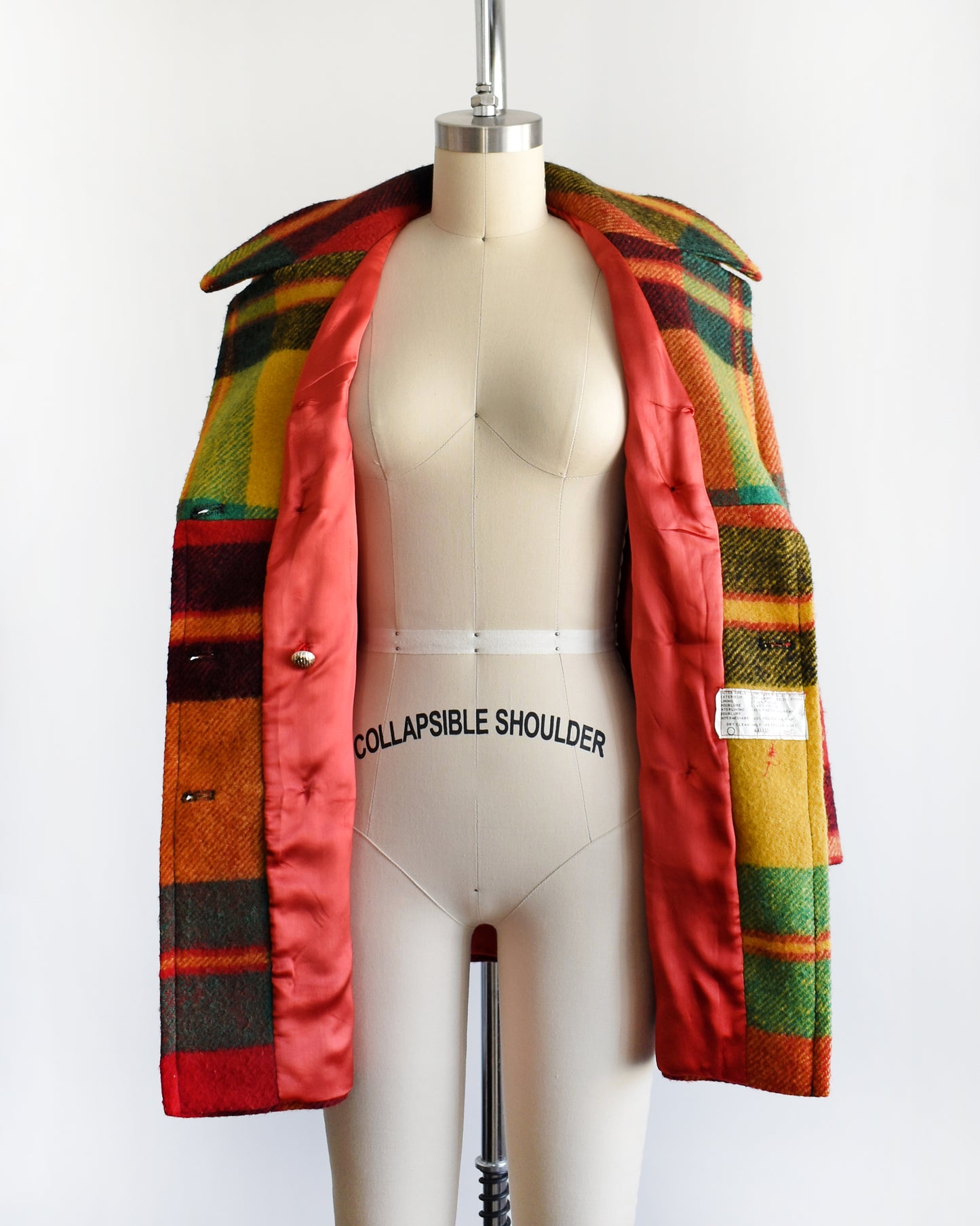 a vintage 1970s rainbow plaid coat on a mannequin against a white background. the coat is open showing the red lining