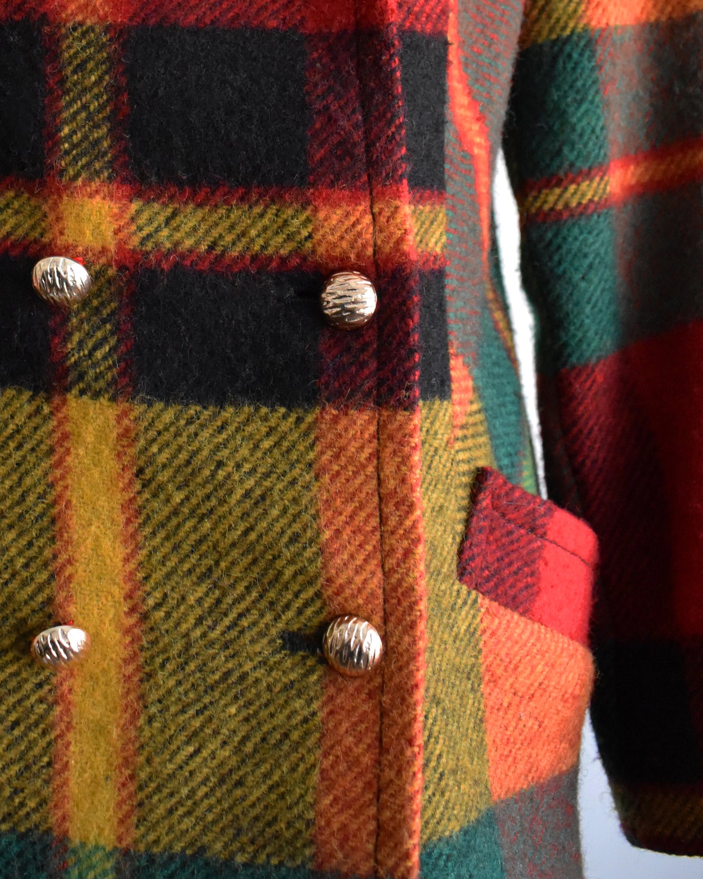 close up of the buttons on a vintage 1970s rainbow plaid coat on a mannequin against a white background