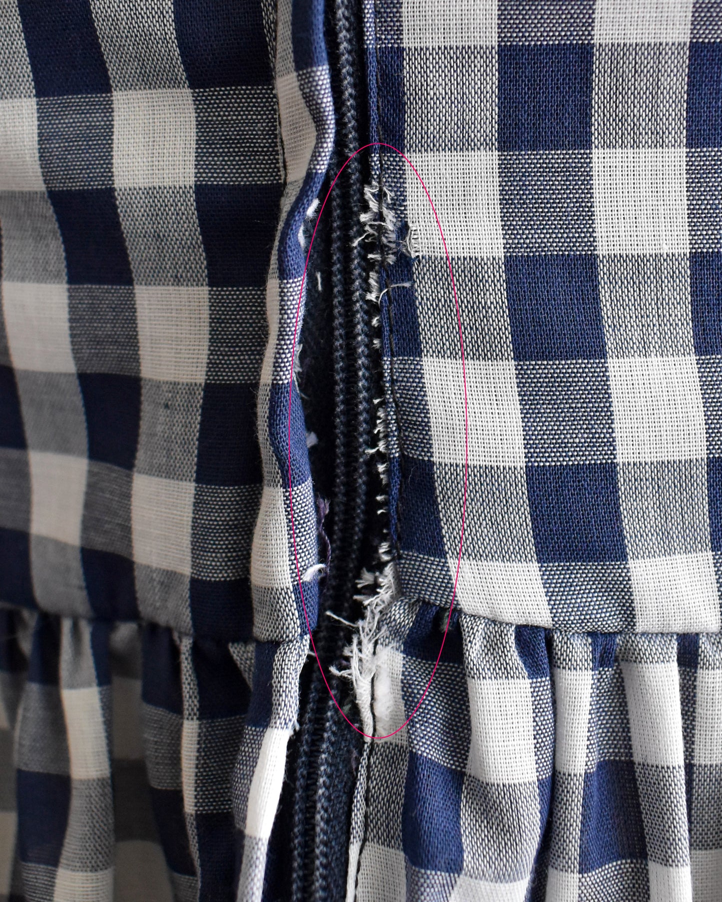 Close-up of a navy and white gingham fabric garment with a frayed seam near the center, highlighted by a pink stitched outline.