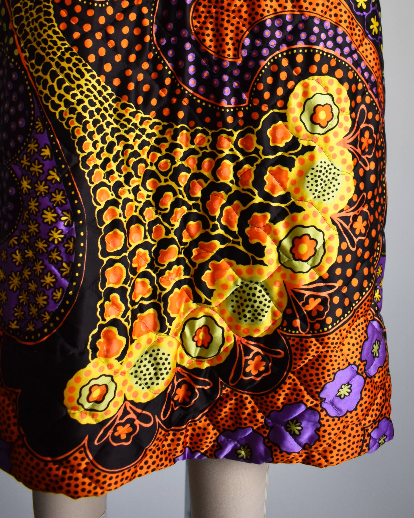 close up of the colorful skirt on a vintage 1970s psychedelic quilted maxi dress on a mannequin against a white background