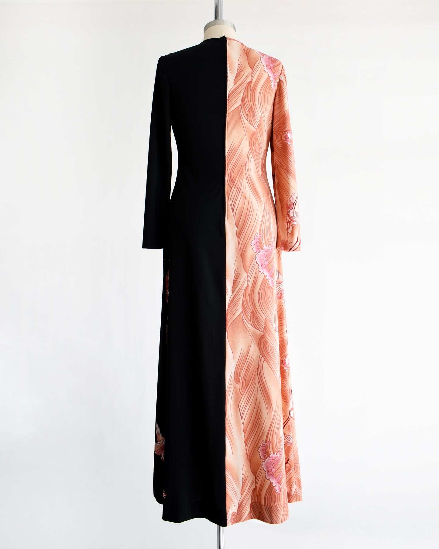 back view of a vintage 1970s dress that has a pink waves and birds on one side and sold black on the other on a mannequin against a white background