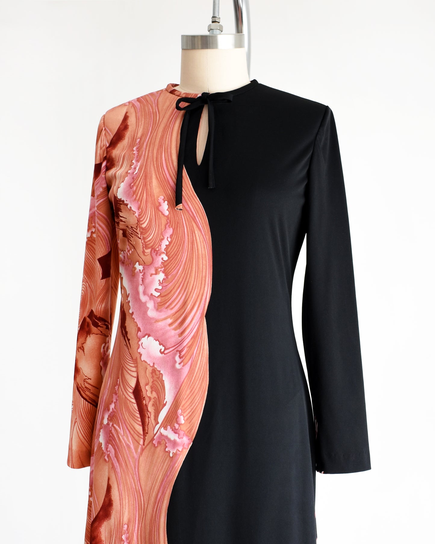 side front view of a vintage 1970s dress that has a pink waves and birds on one side and sold black on the other on a mannequin against a white background
