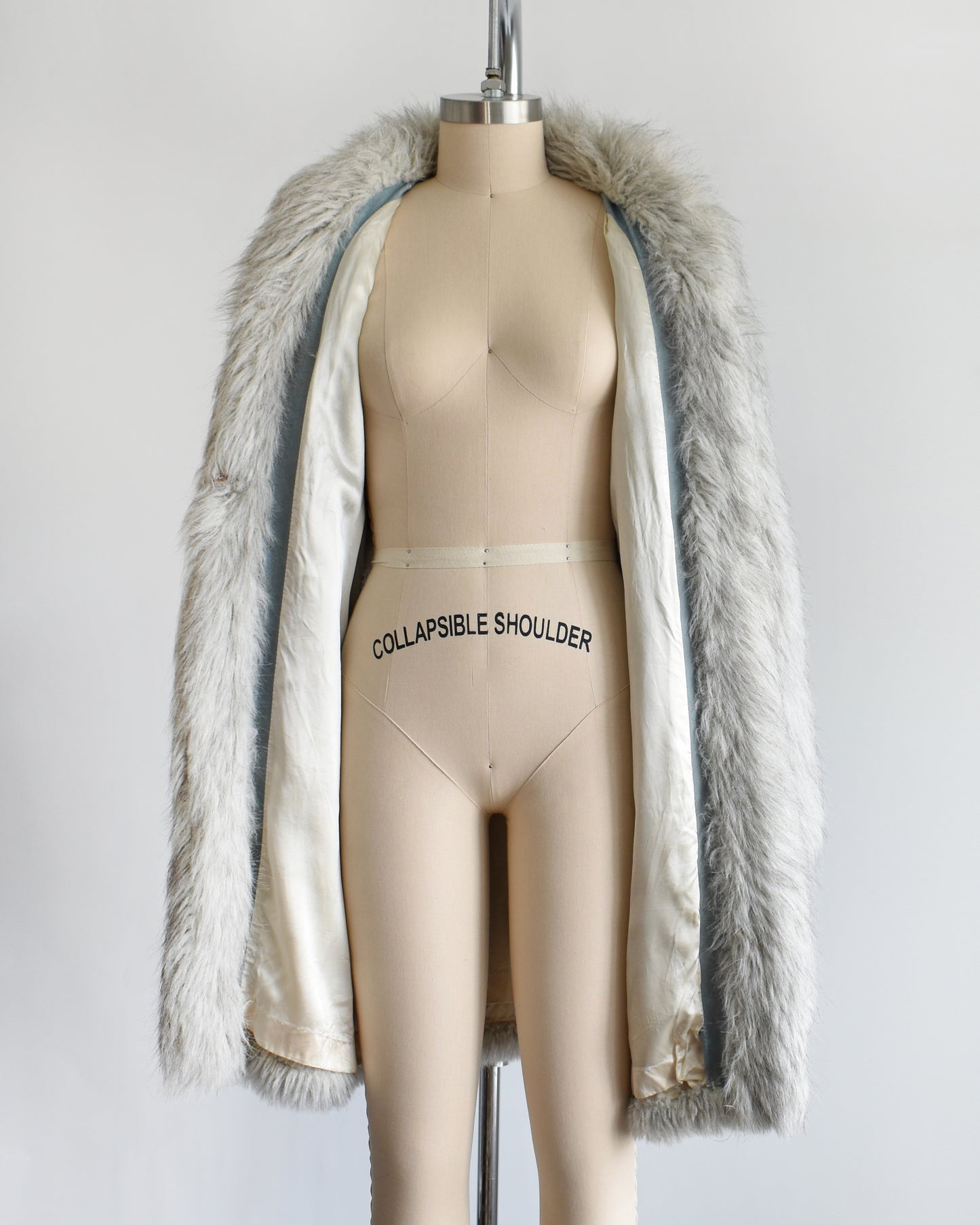 a vintage 1980s faux fur silver fox coat on a dress form on a white background. the coat is open, showing the lining