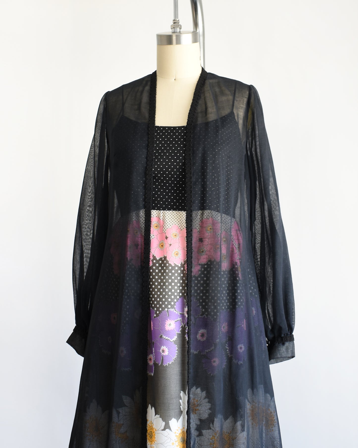 side front view of a vintage 1970s black floral dress with black duster on a mannequin against a white background