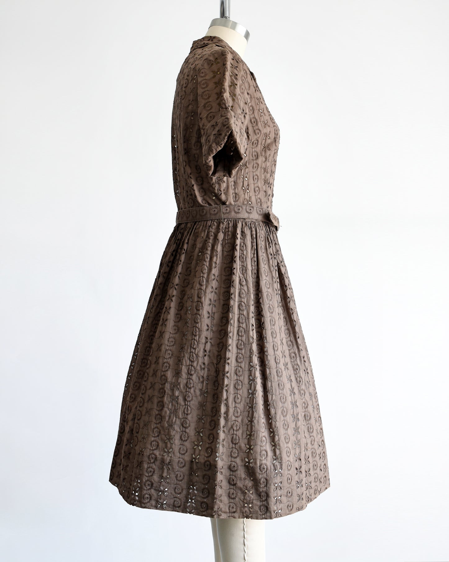 side view of a vintage 1950s brown eyelet shirt dress with belt on a dress form