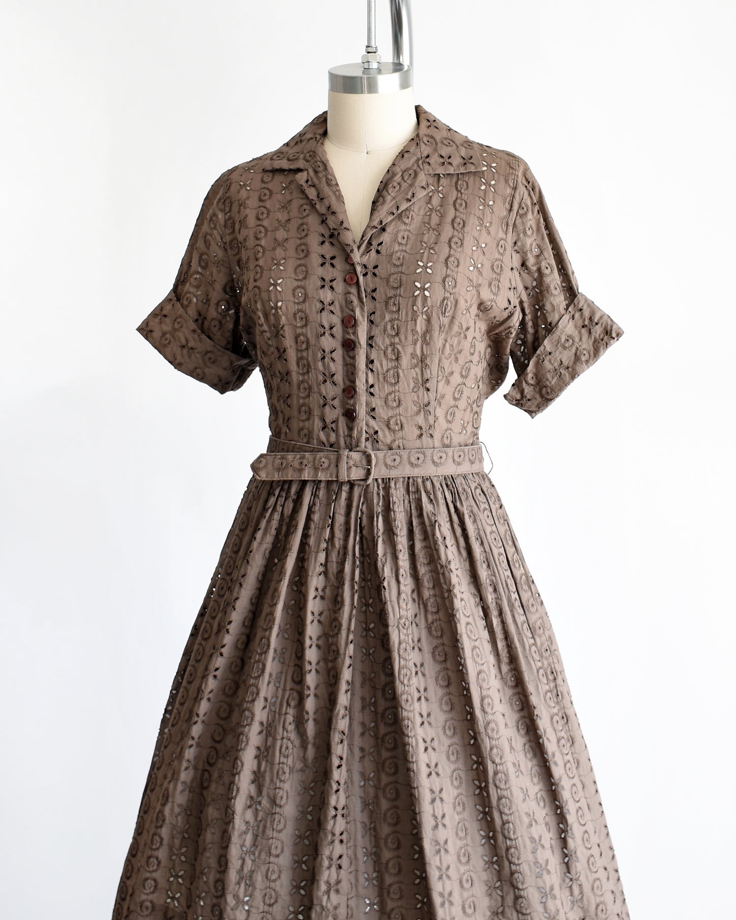 side front view of a vintage 1950s brown eyelet shirt dress with belt on a dress form