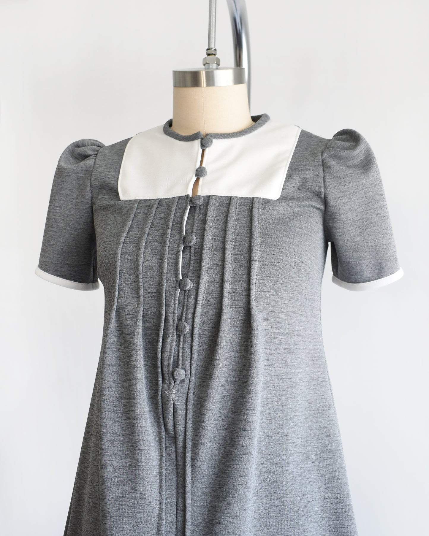side front view of a vintage 1960s gray dress with white collar on a mannequin against a white background