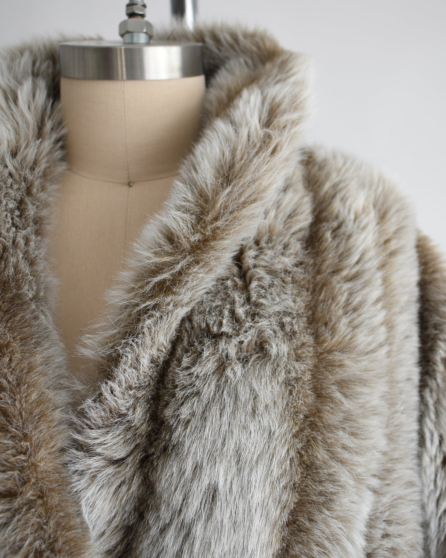 Close-up of a faux fur coat on a mannequin with a plain background