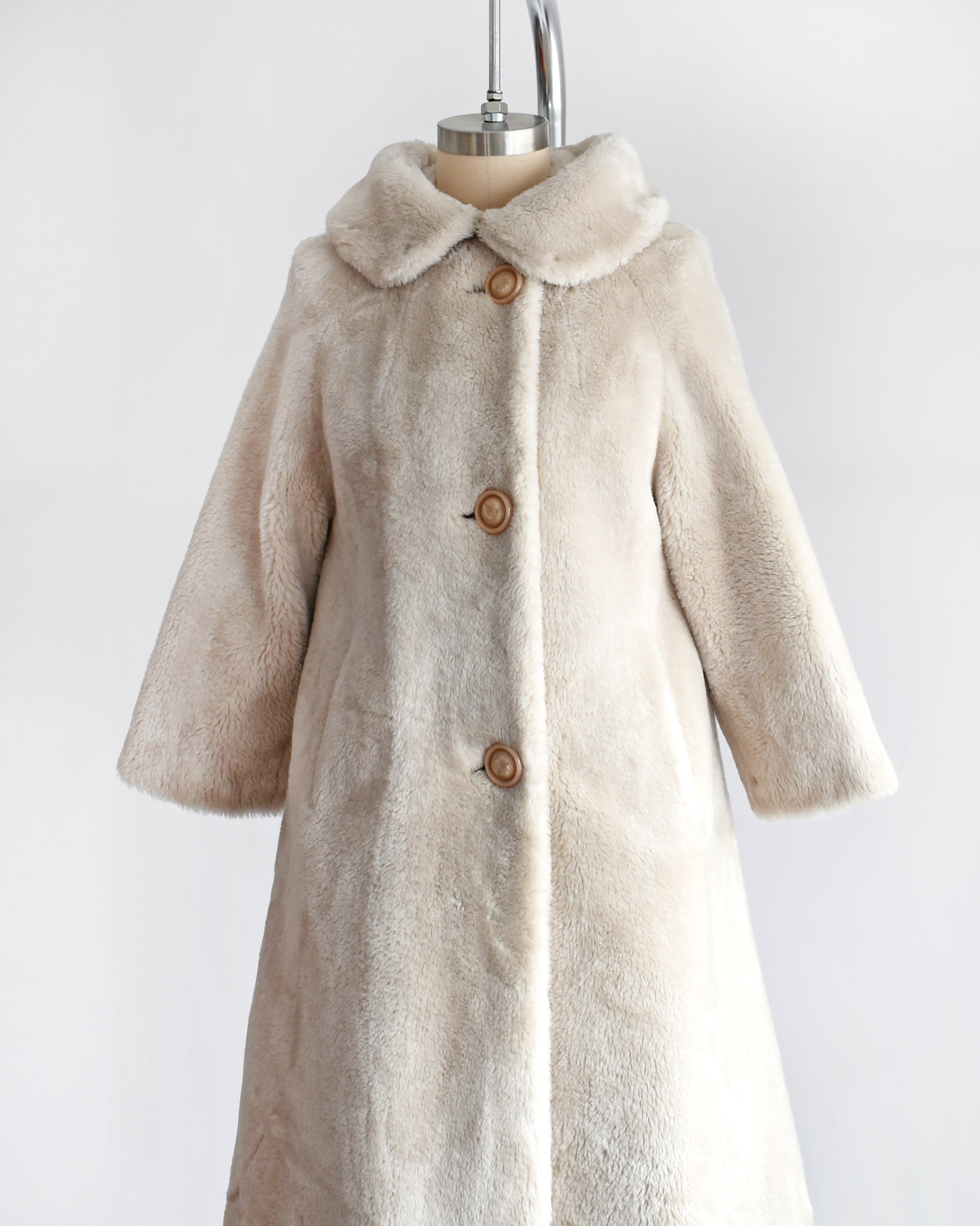 Side front view of a vintage 1960s plush cream faux fur coat that features a Peter Pan style collar and three large buttons down the front