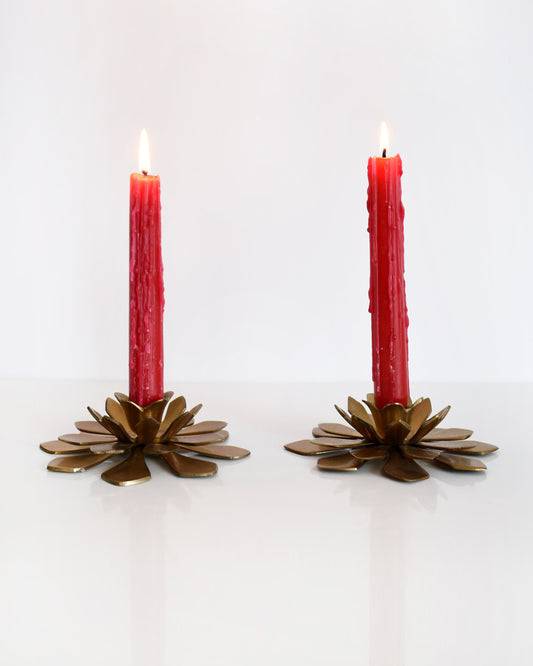 A pair of vintage brass lotus candle holders with red candles on a white table