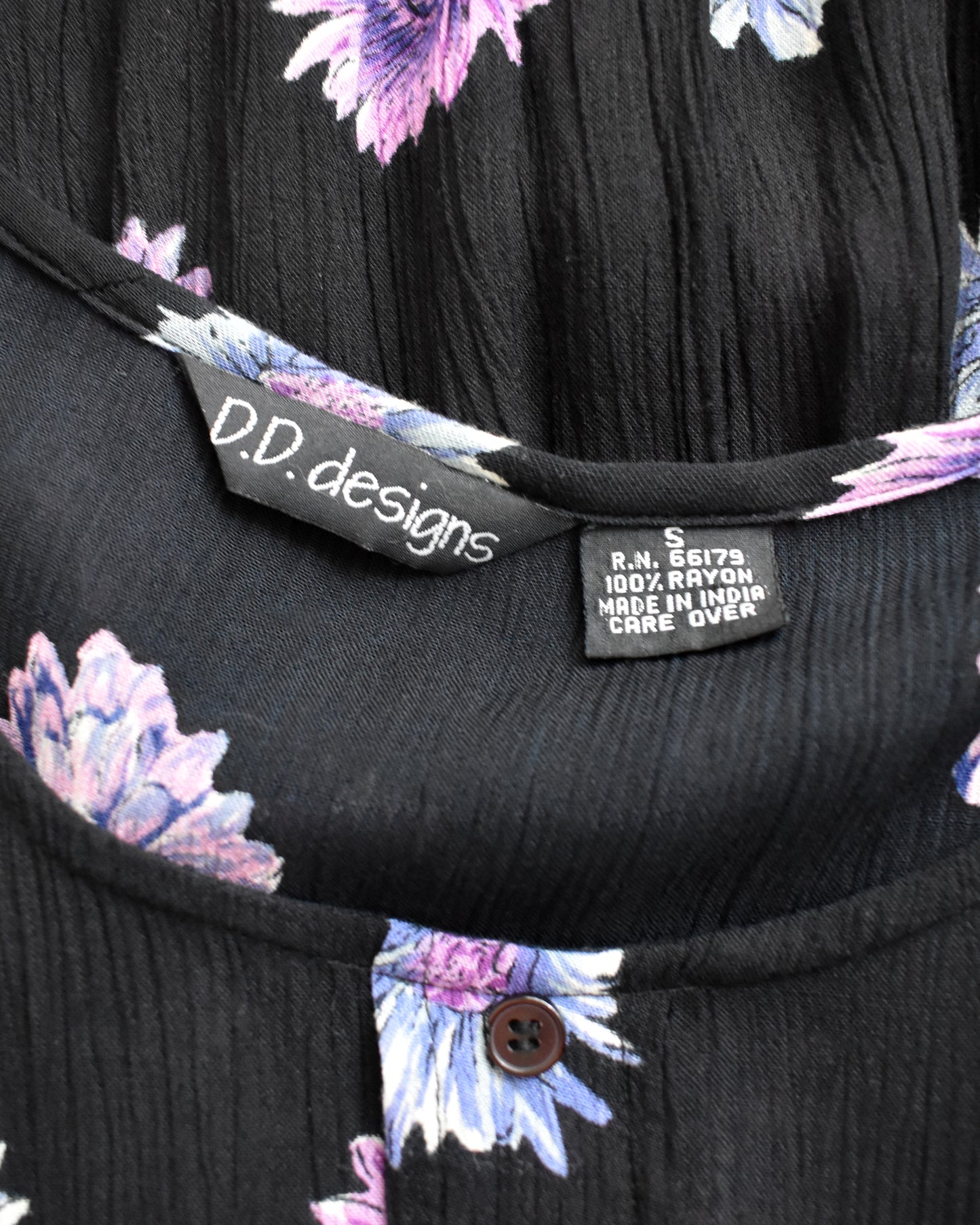 Close-up of a black crinkled dress neckline with a purple and blue floral print, showing the inner neck label 'D.D. designs'.