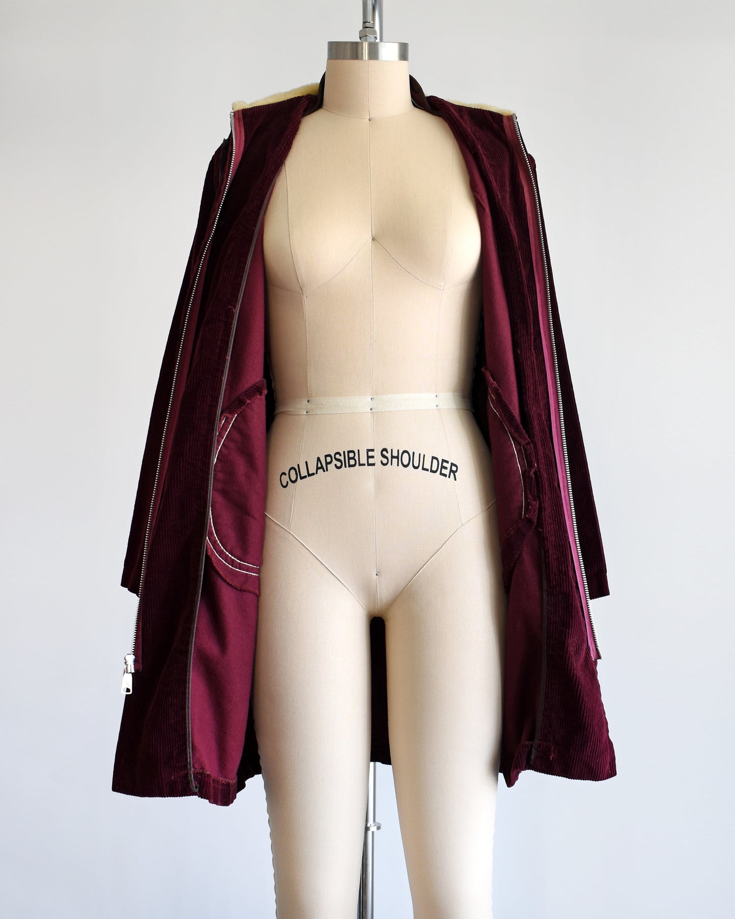 a vintage 1970s burgundy corduroy jacket with a sherpa lined hood on a dress form. The coat is unzipped in this photo.