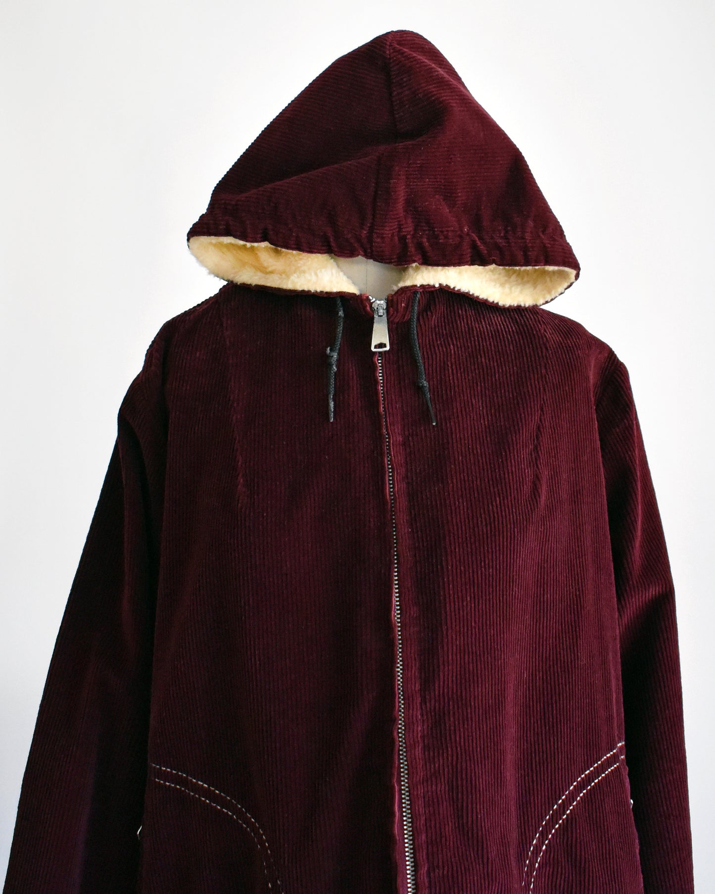 a vintage 1970s burgundy corduroy jacket with a sherpa lined hood on a dress form. the hood is pulled forward in this photo.