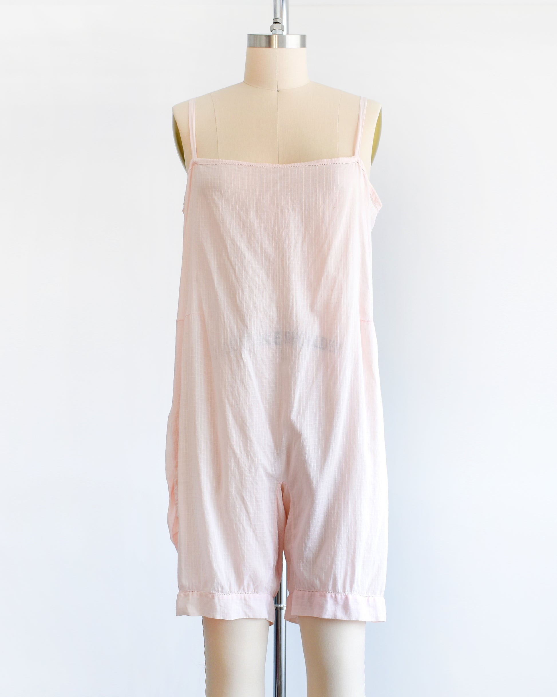 A vintage 1920s light pink chemise step in, which has spaghetti straps, square neckline, and snap buttons on the right side. The garment is on a dress form.