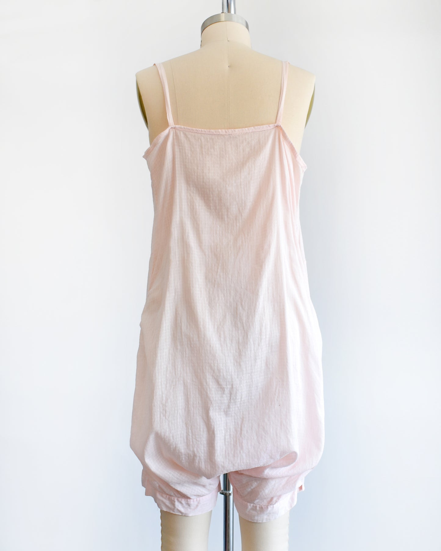 Back view of a vintage 1920s light pink chemise step in, which has spaghetti straps, square neckline, and snap buttons on the right side. The garment is on a dress form.