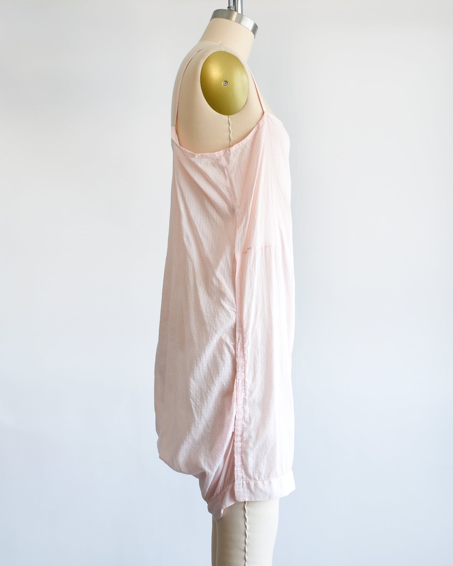 Side view of a vintage 1920s light pink chemise step in, which has spaghetti straps, square neckline, and snap buttons on the right side. The garment is on a dress form.