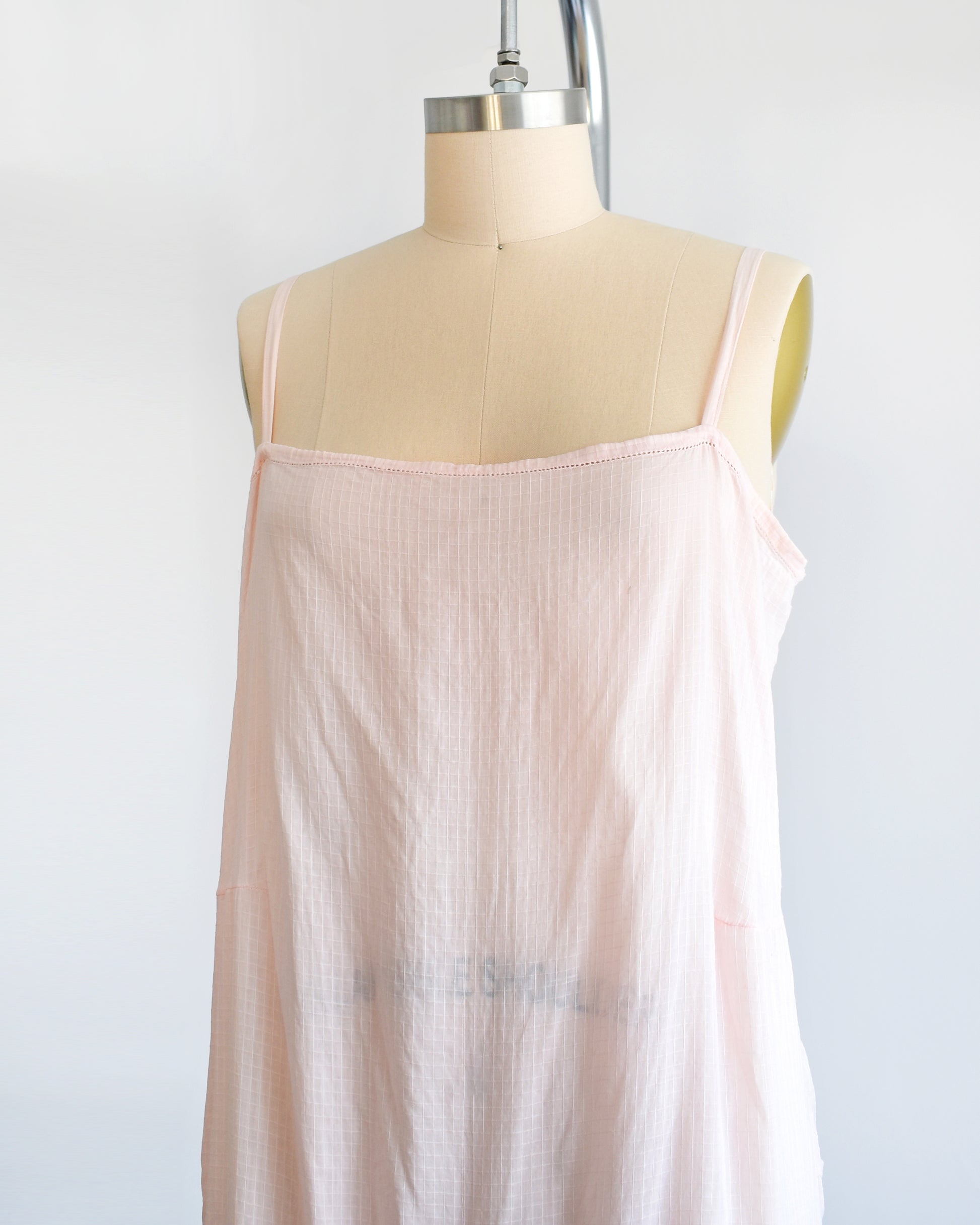 Side front view of a vintage 1920s light pink chemise step in, which has spaghetti straps and square neckline. The garment is on a dress form.