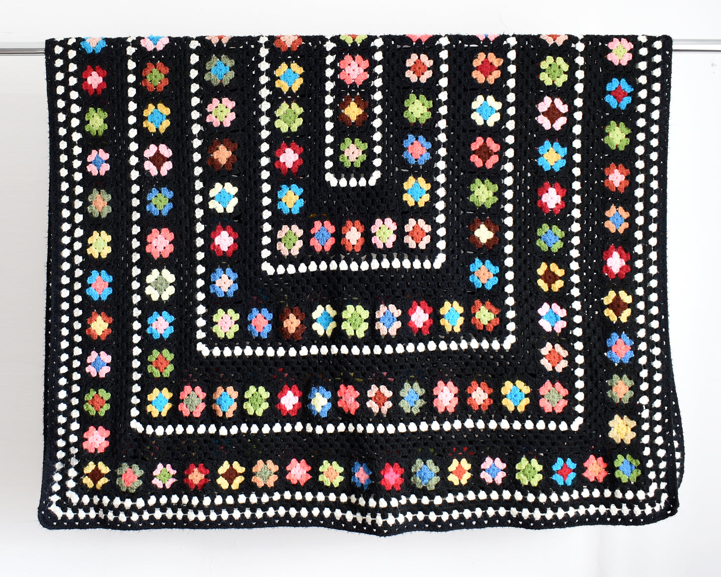 a vintage black and white crochet blanket with a colorful granny square pattern draped over a silver rod
