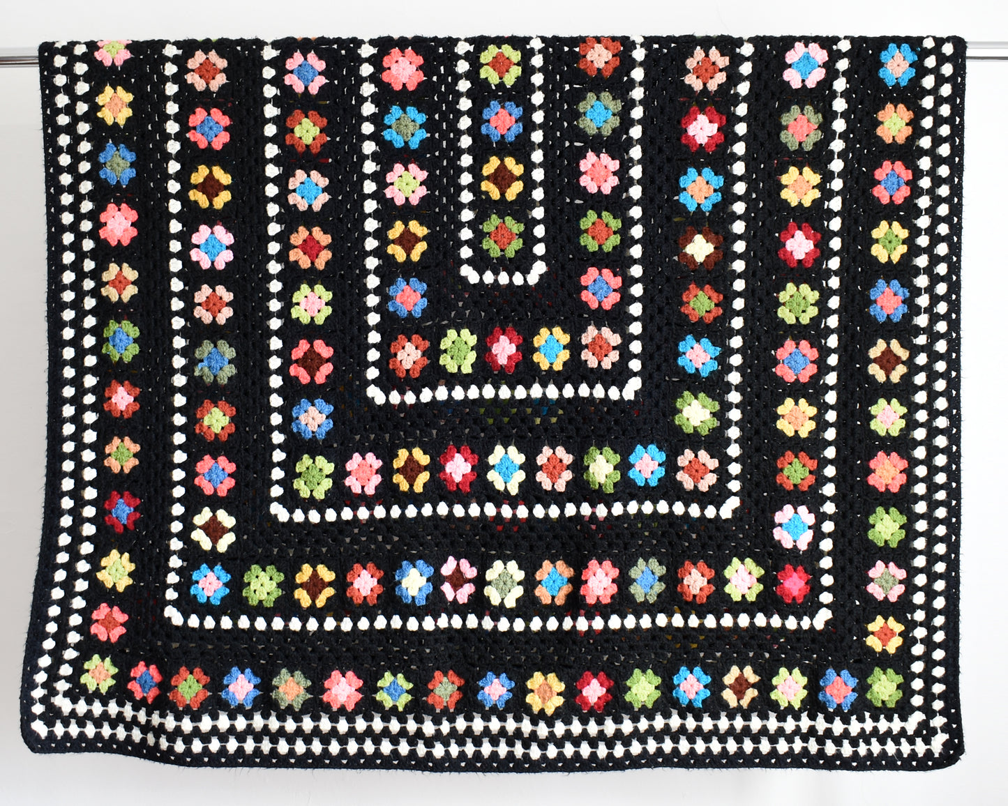 a vintage black and white crochet blanket with a colorful granny square pattern draped over a silver rod