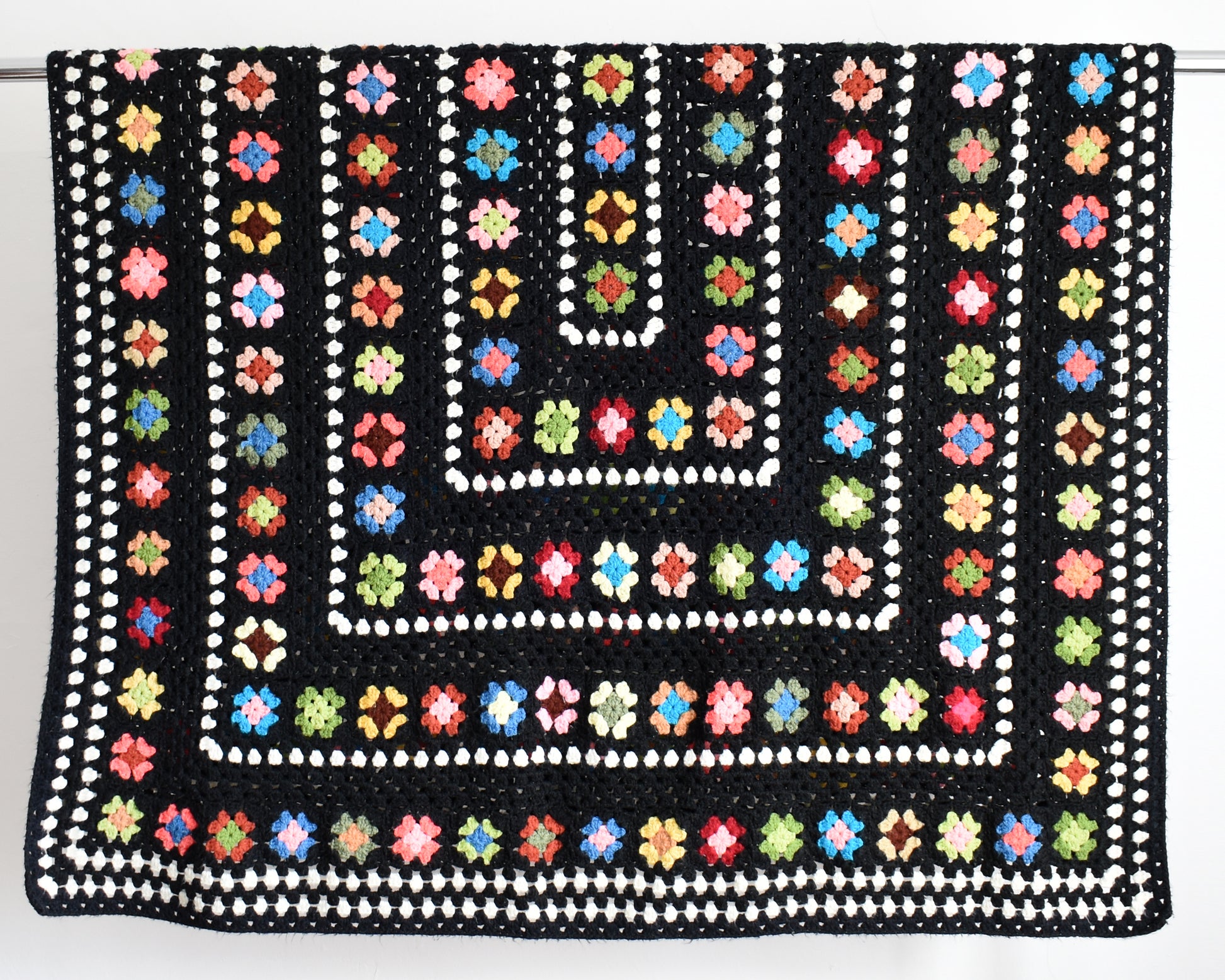 a vintage black and white crochet blanket with a colorful granny square pattern draped over a silver rod