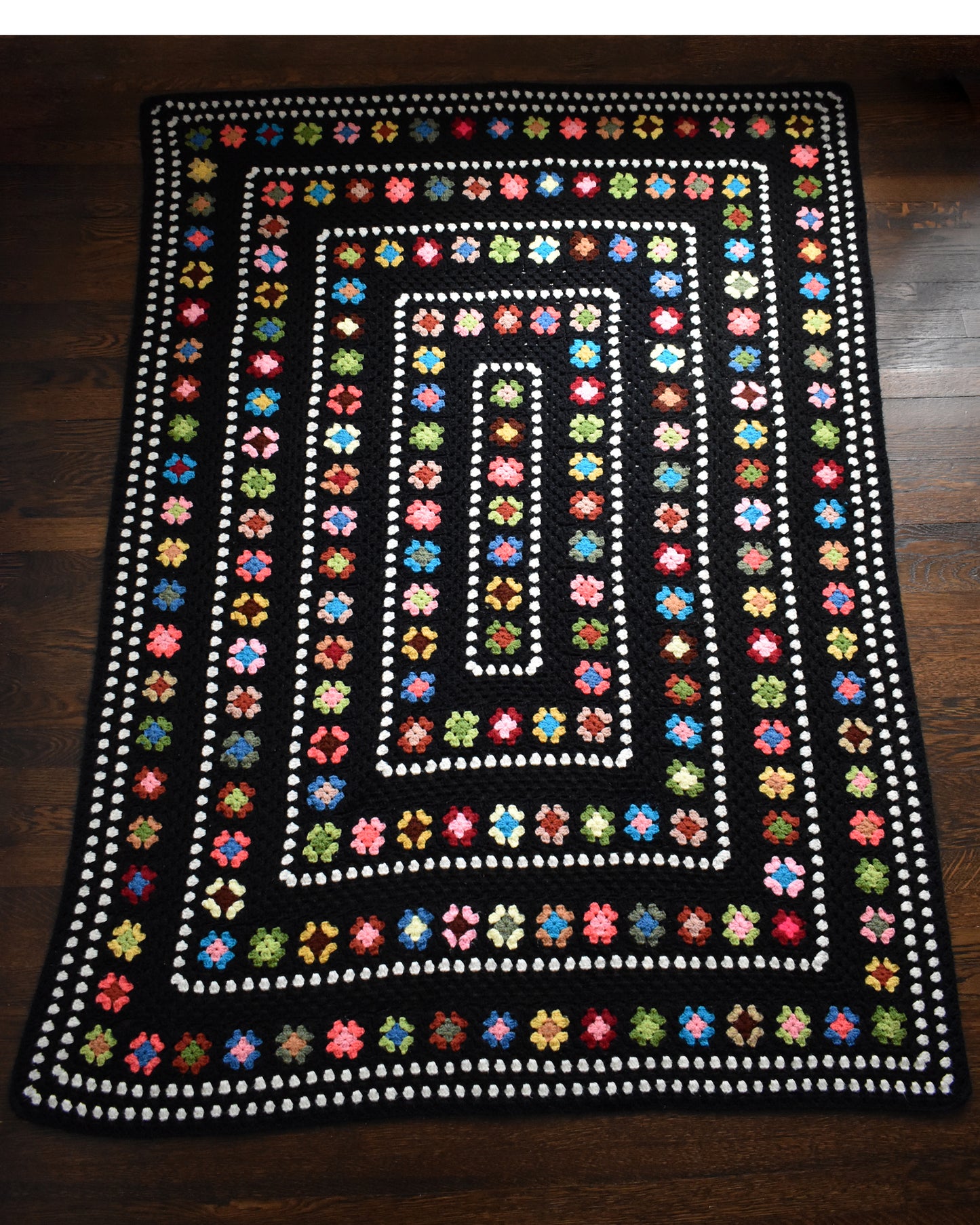a vintage black and white crochet blanket with a colorful granny square pattern laid out on a wood floor