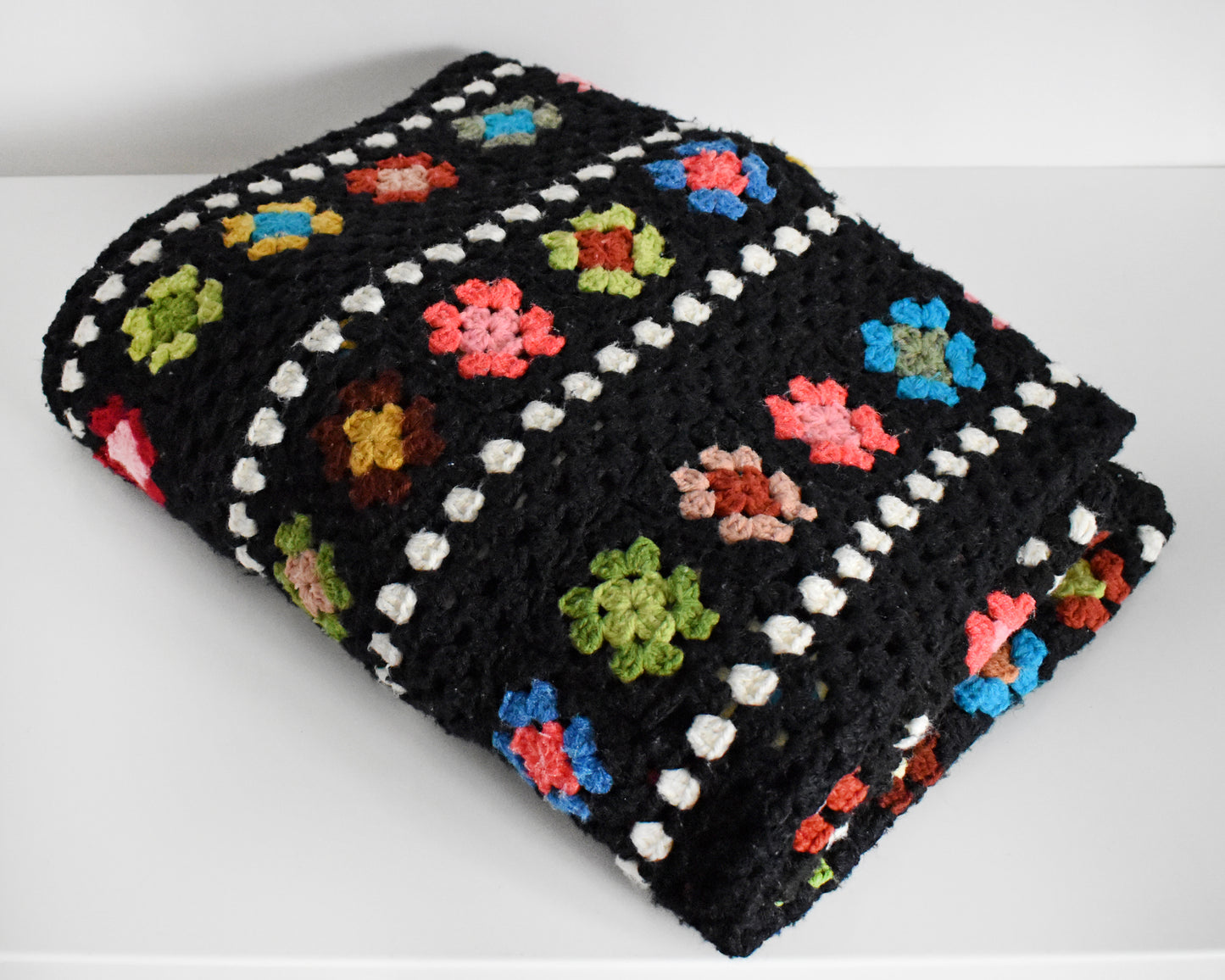 a vintage black and white crochet blanket with a colorful granny square pattern folded on a white table