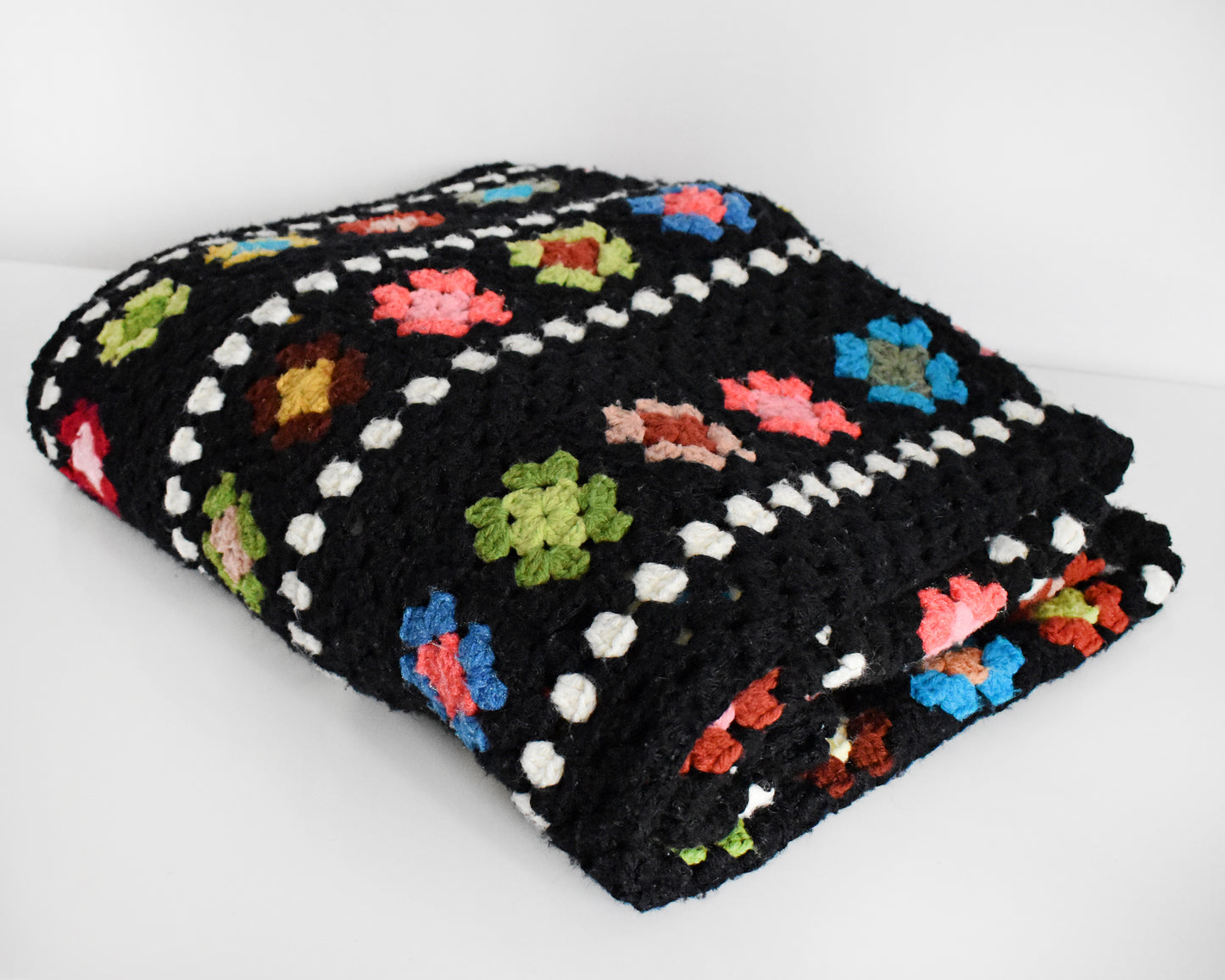 a vintage black and white crochet blanket with a colorful granny square pattern folded on a white table