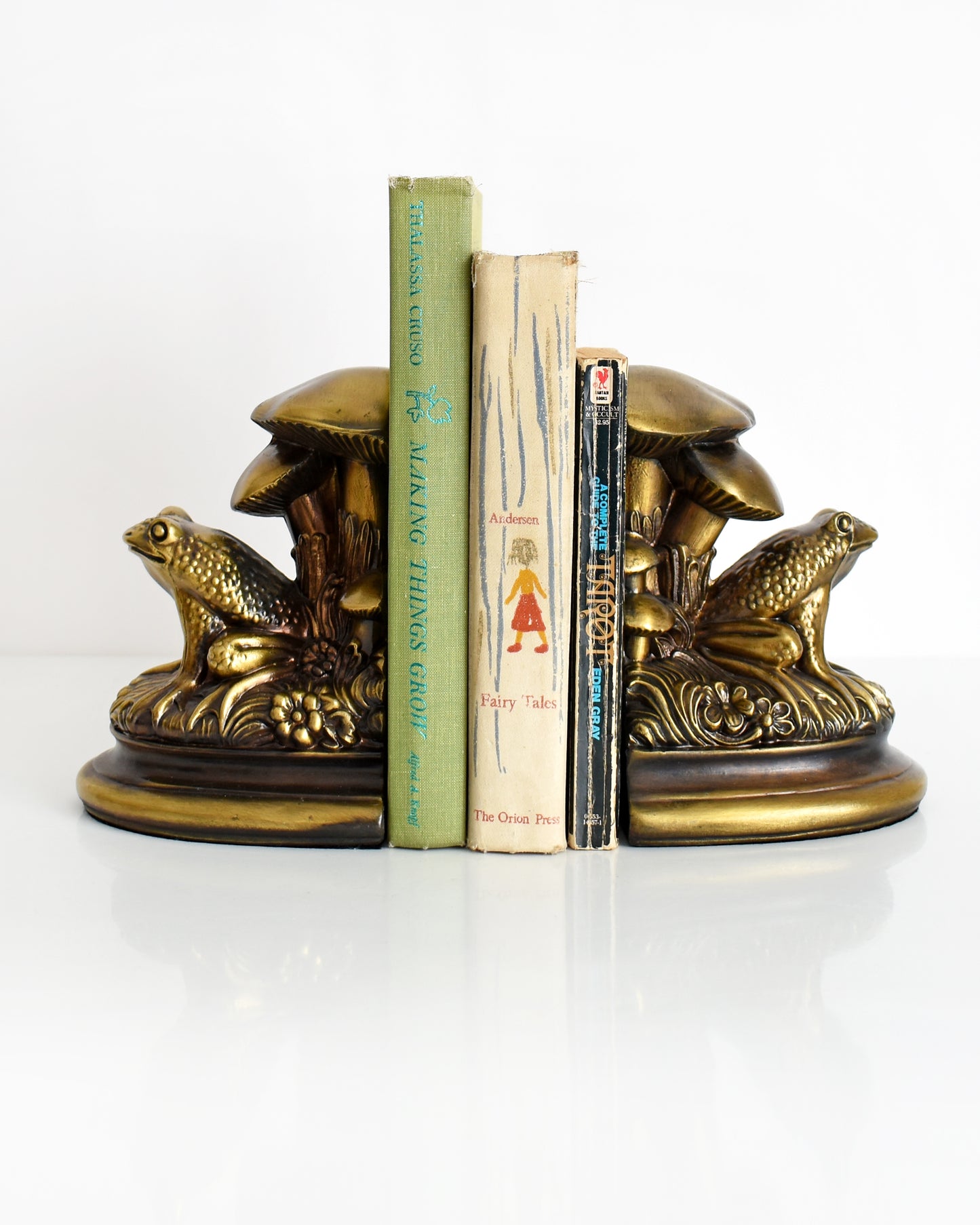 vintage brass frog and mushroom bookends with three books in the middle
