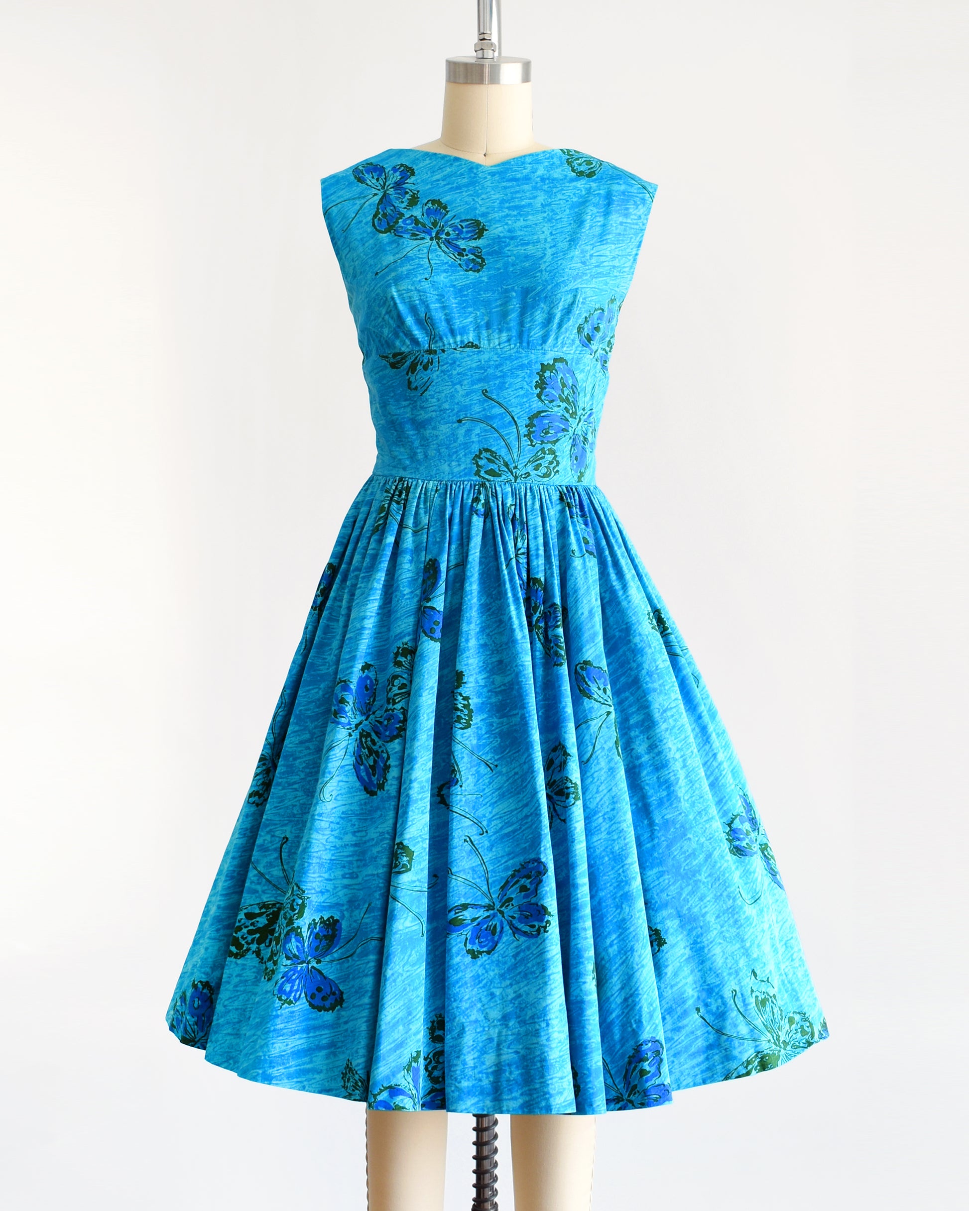A vintage 1950s Anne Fogarty blue fit and flare dress that has a butterfly print. The dress is on a dress form.