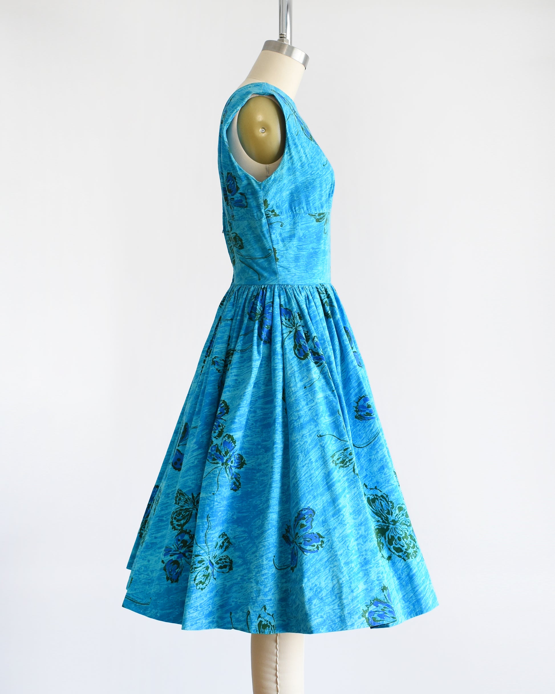 Side view of a vintage 1950s Anne Fogarty blue fit and flare dress that has a butterfly print. The dress is on a dress form.