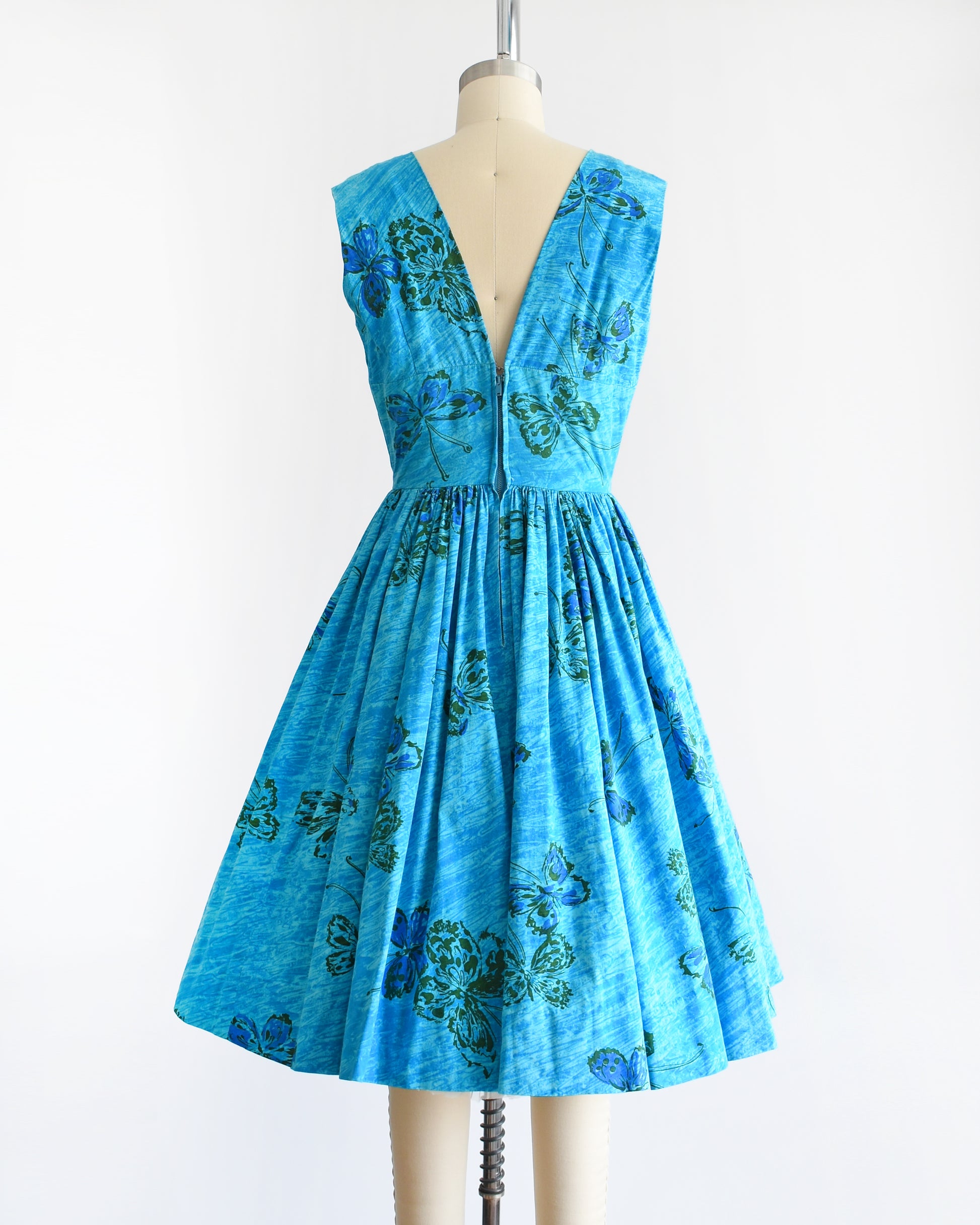 Back view of a vintage 1950s Anne Fogarty blue fit and flare dress that has a butterfly print. The dress is on a dress form.