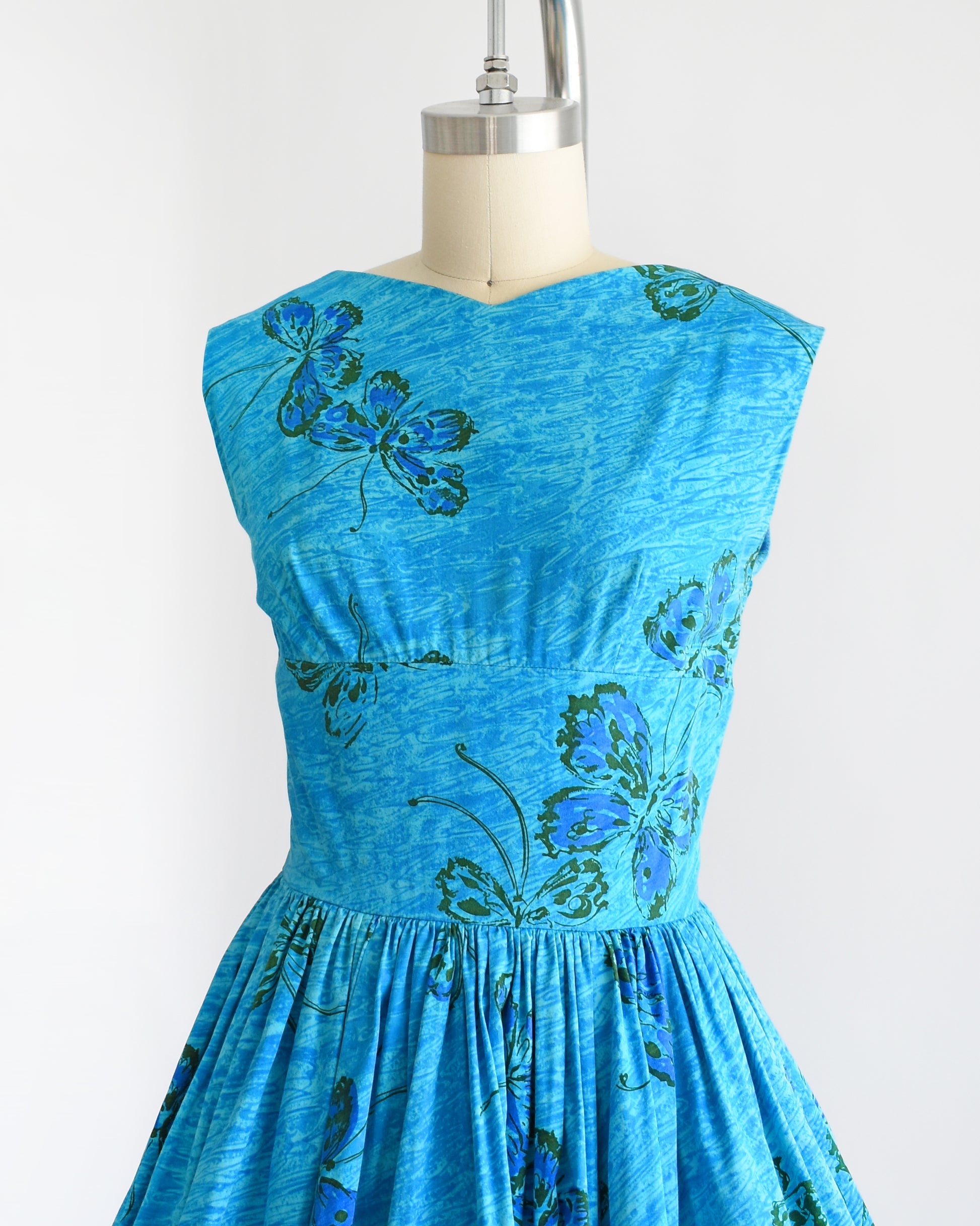 Side front view of a vintage 1950s Anne Fogarty blue fit and flare dress that has a butterfly print. The dress is on a dress form.