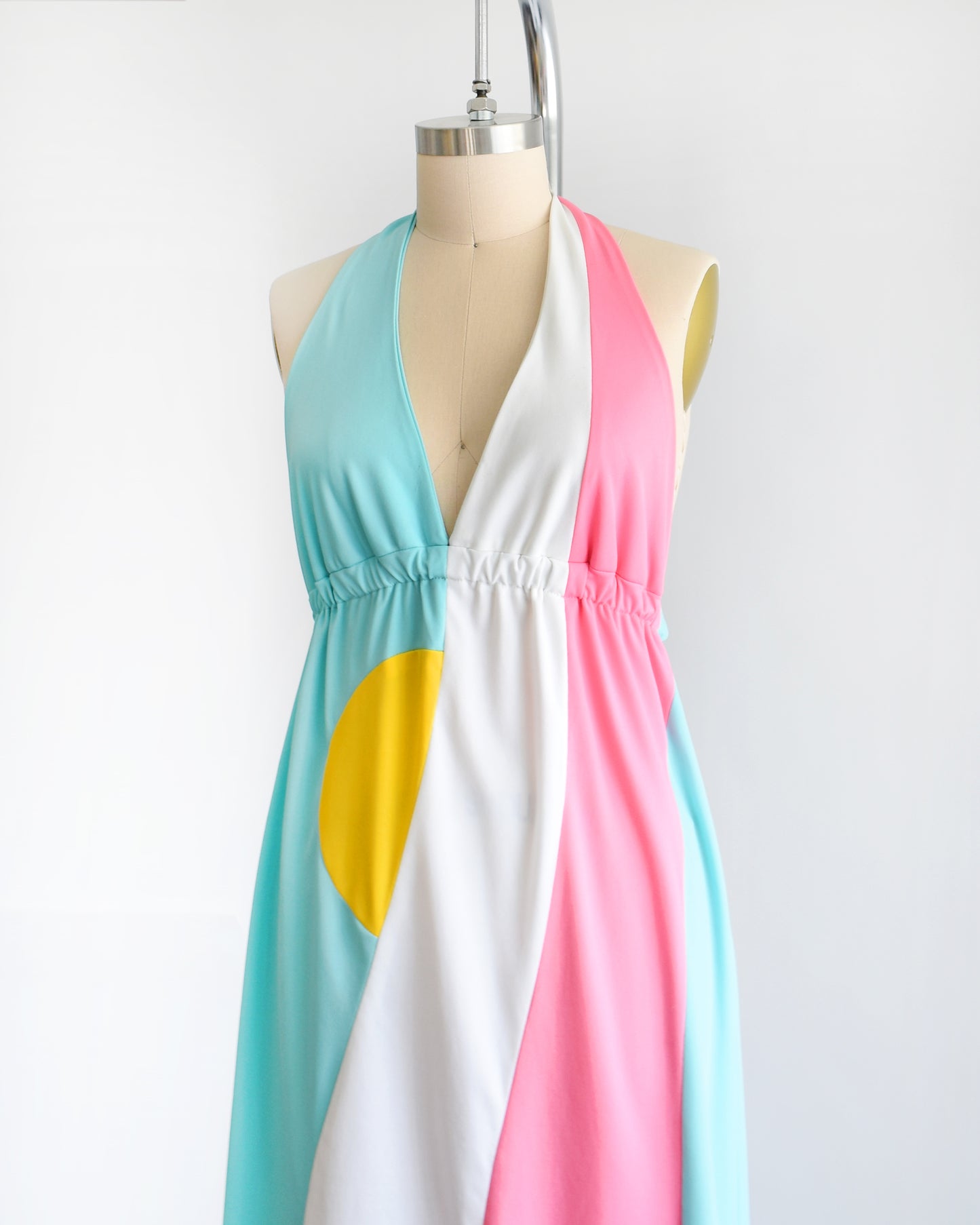 Side front view of a vintage 1970s halter maxi dress that is blue with a white and pink swirl on the side with a half yellow circle peeking out just below the waistband.
