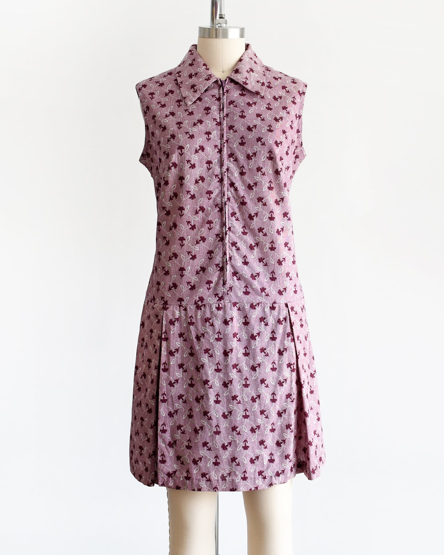 This 1970s vintage romper features a cute purple and white floral print, a collared neckline, and a metal zipper closure down the front.