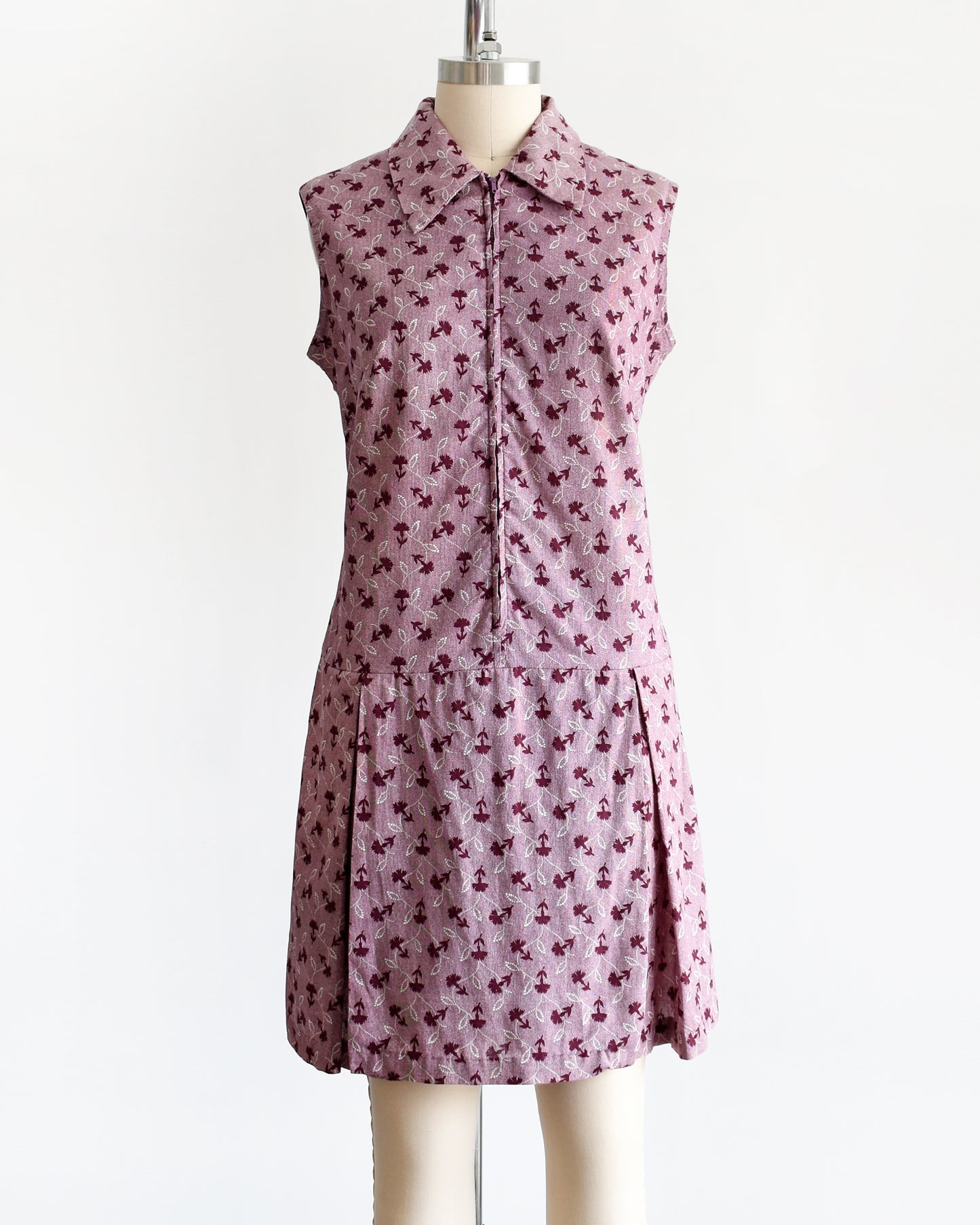 This 1970s vintage romper features a cute purple and white floral print, a collared neckline, and a metal zipper closure down the front. 
