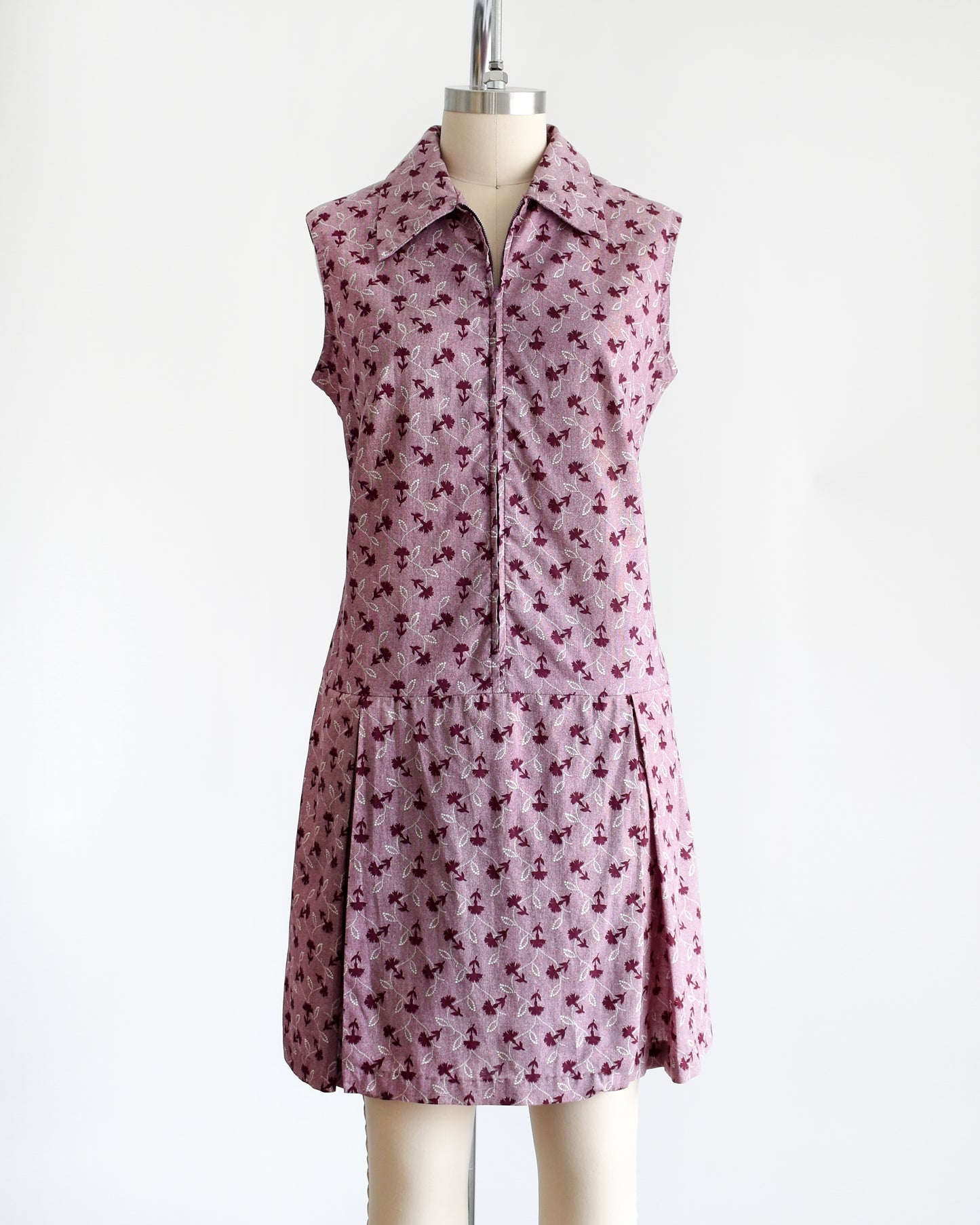This 1970s vintage romper features a cute purple and white floral print, a collared neckline, and a metal zipper closure down the front. The zipper is unzipped slightly in this photo.