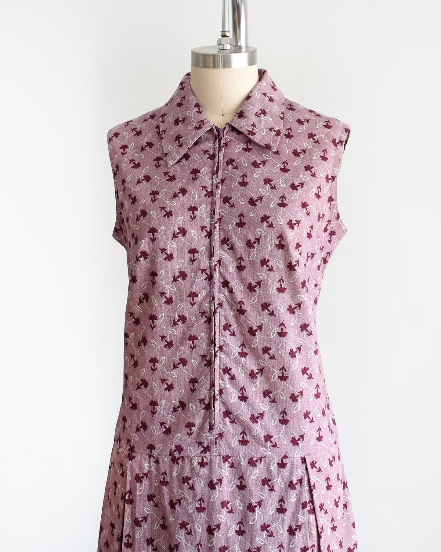 Side front view of a 1970s vintage romper features a cute purple and white floral print, a collared neckline, and a metal zipper closure down the front.
