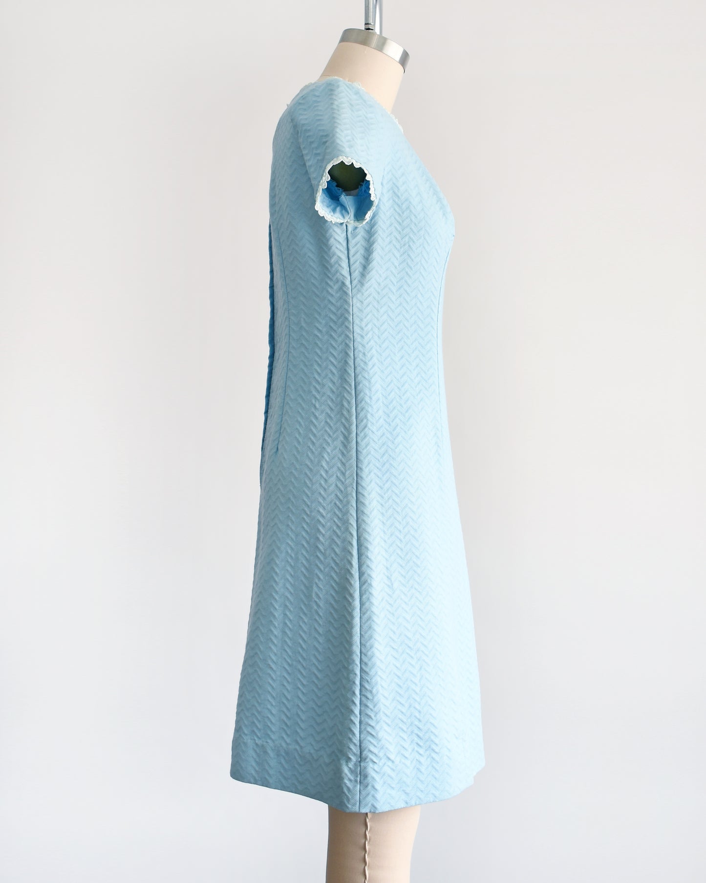 Side view of a A vintage 1960s mod dress that has textured light blue chevron striped knit with alternating ribbing and lace trim.