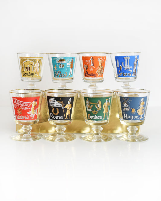 This Libbey International Set features 8 mid century city colorful glasses with distinct scenes, metallic gold/white accents. The top row is Bombay, Paris, Havana, Athens and they sit on a gold box. The bottom row is Madrid, Rome, London, The Hague